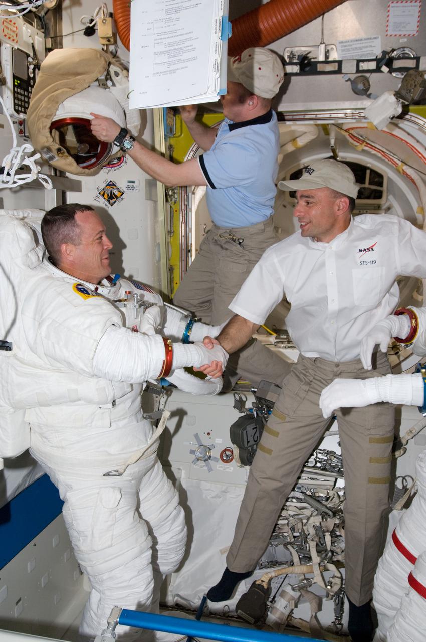 ISS018-E-041237 (19 March 2009) --- Astronaut Richard Arnold, STS-119 mission specialist, attired in his Extravehicular Mobility Unit (EMU) spacesuit, and astronaut Lee Archambault, STS-119 commander, shake hands in the Quest Airlock of the International Space Station as the mission's first scheduled session of extravehicular activity (EVA) draws to a close. Astronaut Michael Fincke, Expedition 18 commander, is visible at top.