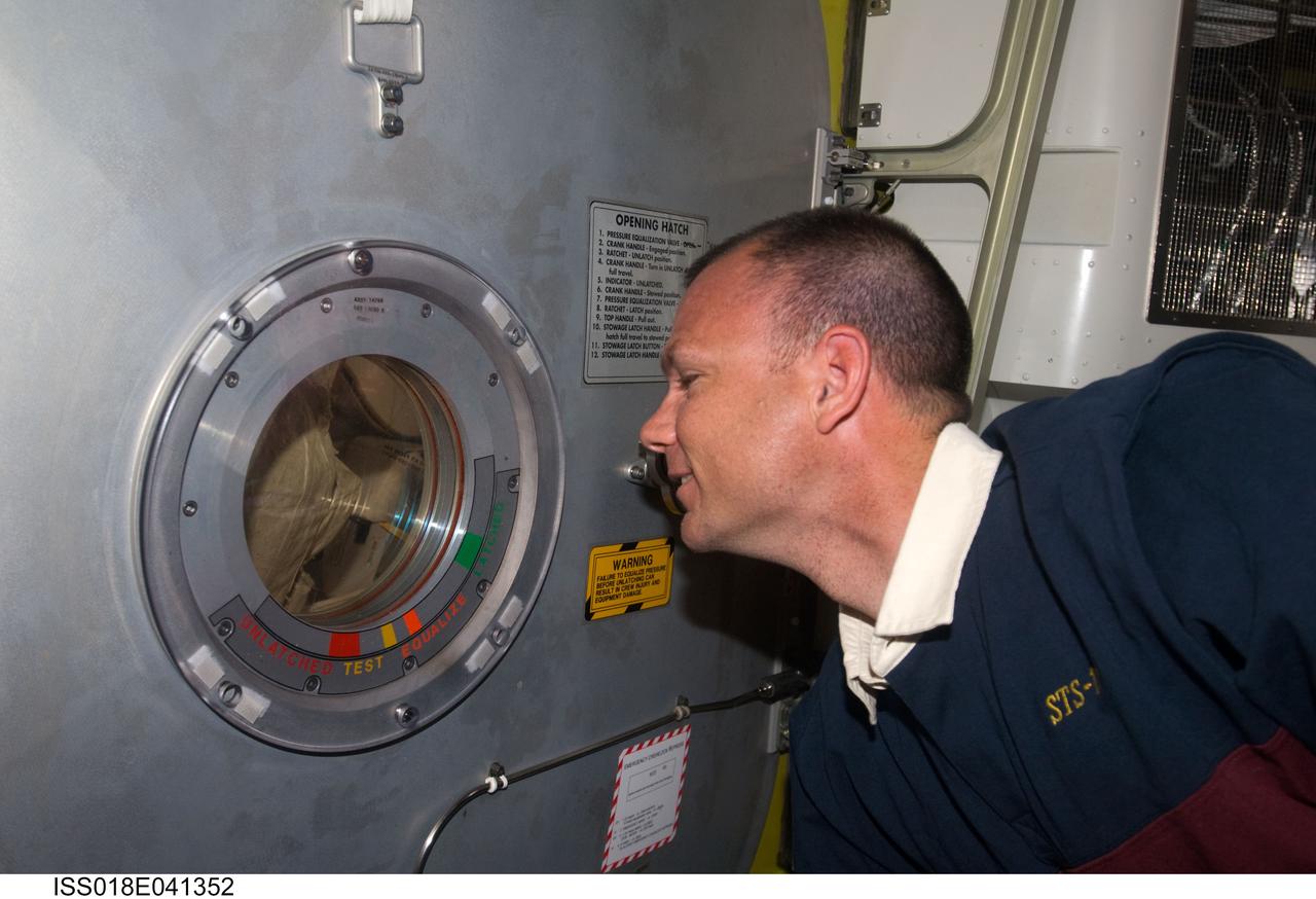 ISS018-E-041352 (21 March 2009) --- Astronaut Tony Antonelli, STS-119 pilot, watches his crewmates through a small window on the hatch door in the Quest Airlock of the International Space Station while Space Shuttle Discovery remains docked with the station. Astronauts Joseph Acaba and Steve Swanson, both STS-119 mission specialists, were exiting the airlock to begin the mission's second session of extravehicular activity (EVA).