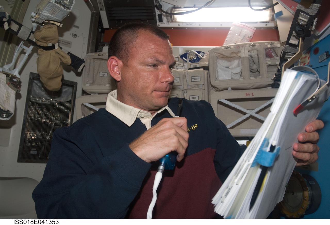ISS018-E-041353 (21 March 2009) --- Astronaut Tony Antonelli, STS-119 pilot, uses a communication system while referring to a checklist in the Quest Airlock of the International Space Station while Space Shuttle Discovery remains docked with the station.