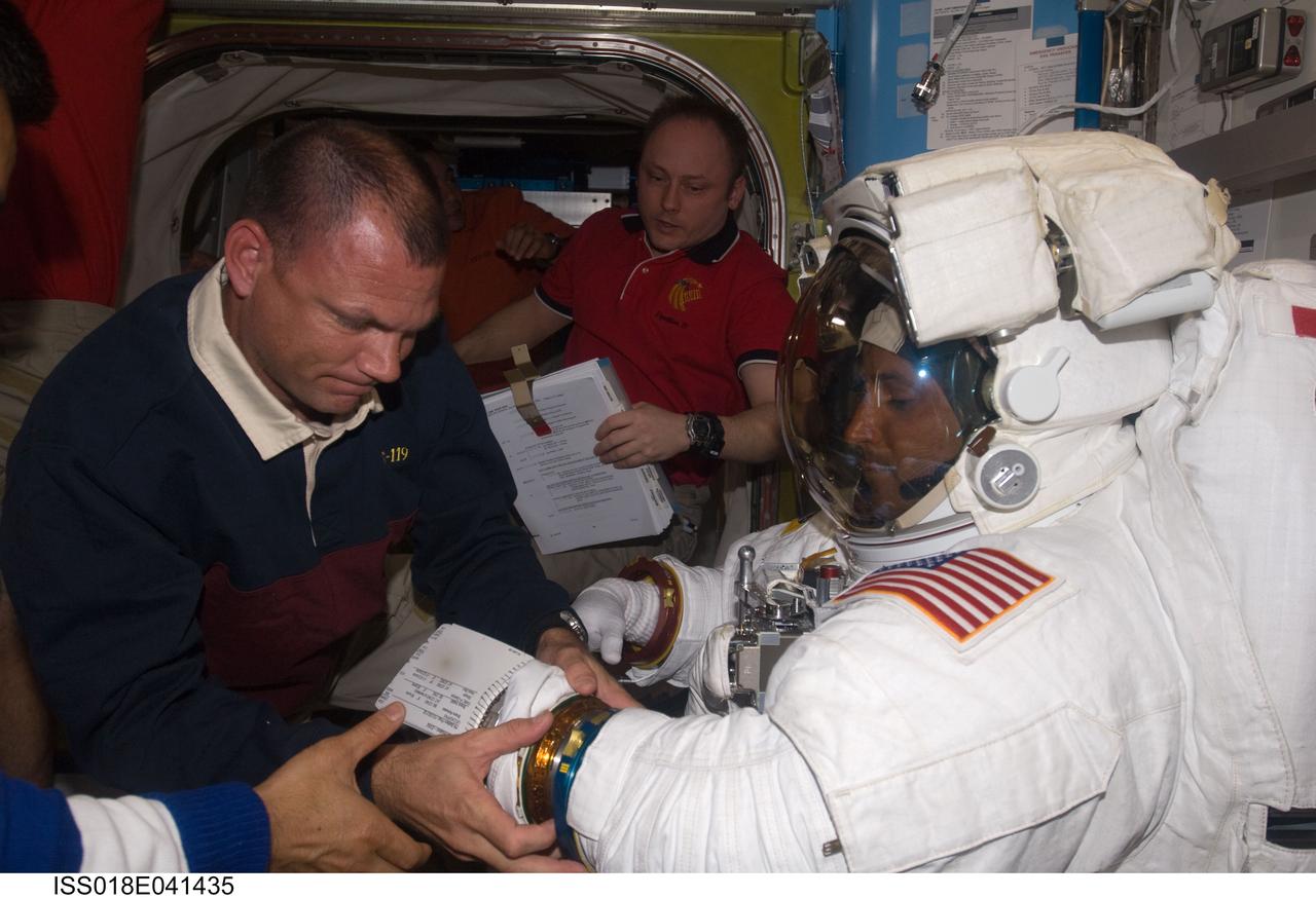 ISS018-E-041435 (21 March 2009) --- Attired in his Extravehicular Mobility Unit (EMU) spacesuit, astronaut Joseph Acaba, STS-119 mission specialist, is pictured in the Quest Airlock of the International Space Station as the mission's second session of extravehicular activity (EVA) draws to a close. Astronaut Tony Antonelli, STS-119 pilot, assists with the doffing of the spacesuit. Astronaut Michael Fincke, Expedition 18 commander, is visible in the background.
