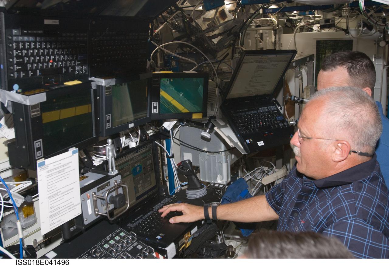ISS018-E-041496 (20 March 2009) --- Astronauts John Phillips (foreground) and Richard Arnold, both STS-119 mission specialists, work the controls of the station's robotic Canadarm2 in the Destiny laboratory of the International Space Station while Space Shuttle Discovery remains docked with the station.