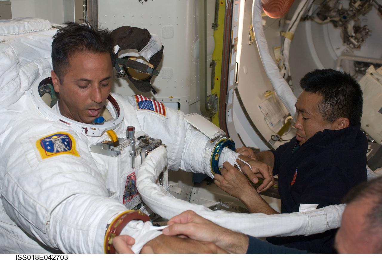 ISS018-E-042703 (23 March 2009) --- Astronaut Joseph Acaba, STS-119 mission specialist, attired in his Extravehicular Mobility Unit (EMU) spacesuit, prepares for the mission's third session of extravehicular activity (EVA) in the Quest Airlock of the International Space Station while Space Shuttle Discovery remains docked with the station. Astronauts Tony Antonelli (bottom right, mostly out of frame), STS-119 pilot; and Japan Aerospace Exploration Agency?s (JAXA) Koichi Wakata, Expedition 18 flight engineer, assist Acaba.
