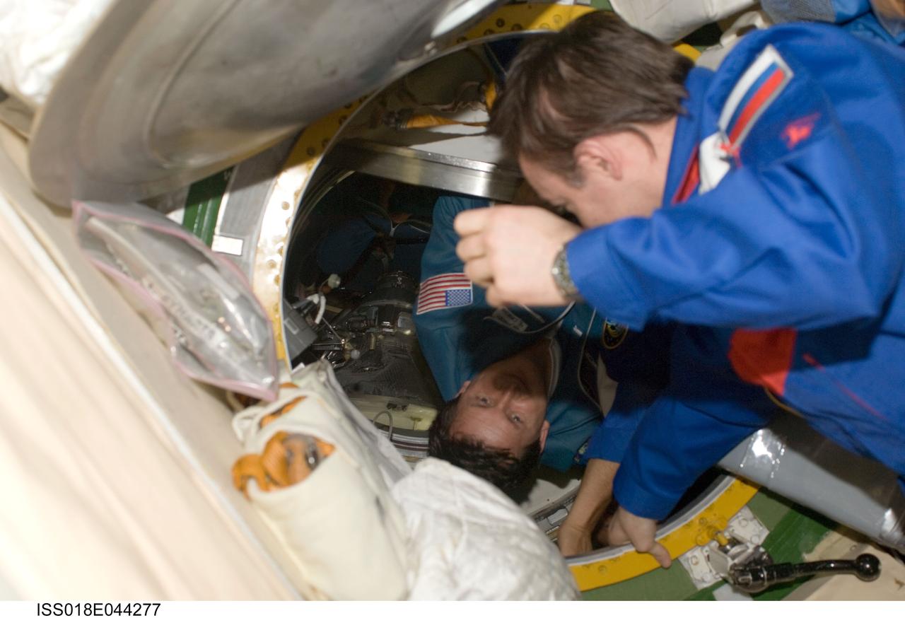 ISS018-E-044277 (28 March 2009) --- Astronaut Michael Fincke (foreground), Expedition 18 commander, welcomes U.S. spaceflight participant Charles Simonyi as he ingresses the International Space Station after arriving onboard a Soyuz spacecraft with two Expedition 19 crewmembers (out of frame).