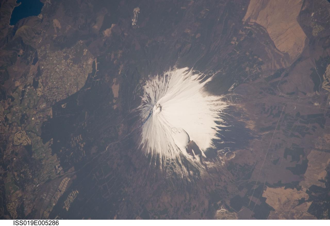 ISS019-E-005286 (8 April 2009) --- Mount Fuji, Japan is featured in this image photographed by an Expedition 19 crew member on the International Space Station. The 3,776 meters high Mount Fuji volcano, located on the island of Honshu in Japan, is one of the world?s classic examples of a stratovolcano. The volcano?s steep, conical profile is the result of numerous interlayered lava flows and explosive eruption products ? such as ash, cinders, and volcanic bombs ? building up the volcano over time. The steep profile is possible because of the relatively high viscosity of the volcanic rocks typically associated with stratovolcanoes. This leads to thick sequences of lava flows near the eruptive vent that build the cone structure, rather than low viscosity flows that spread out over the landscape and build lower-profile shield volcanoes. According to scientists, Mount Fuji, or Fuji-san in Japan, is actually comprised of several overlapping volcanoes that began erupting in the Pleistocene Epoch (1.8 million to approximately 10,000 years ago). Scientists believe that the currently active volcano, known as Younger Fuji, began forming approximately 11,000 to 8,000 years ago. The most recent explosive activity occurred in 1707, creating Hoei Crater on the southeastern flank of the volcano (center). This eruption deposited ash on Edo (present-day Tokyo) located 95 kilometers to the northeast. While there have been no further eruptions of Mount Fuji, steam was observed at the summit during 1780?1820, and the volcano is considered active. This oblique photograph illustrates the snow-covered southeastern flank of the volcano; the northeastern flank can be seen here. A representation of the topography of Mt. Fuji and its surroundings can be viewed here.