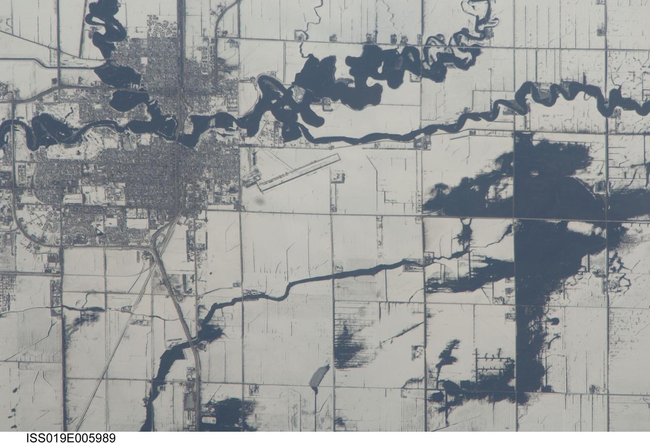 ISS019-E-005989 (9 April 2009) --- Red River floods in North Dakota and Minnesota are featured in this image photographed by an Expedition 19 crewmember on the International Space Station. The Red River, which flows north between North Dakota and Minnesota, flooded for a second time on the day this image was taken (9 April 2009). Two weeks earlier the river had crested at very high levels. The new floodwaters in the Red River, and especially in the less well-drained meandering tributaries east of the river, appear as black shapes against a snowy agricultural landscape defined by rectangular fields. The largest irregular black patches are the flooded low parts of fields along a canalized western tributary of the Red River (right). The city-block patterns of Wahpeton ND and Breckenridge MN, opposite one another on the banks of the Red River, stand out as dark gray patches against the snow at image top left. The main runway of the Henry Stern Airport lies angled northwest directly south of Wahpeton, and its 1.3 kilometers runway length gives scale to the view. Access roads to the agricultural fields tend to follow an orthogonal pattern, while larger roads leading to the cities cut across this pattern (lower left, near Wahpeton). A subtle pattern of drainage ditches and plow lines appear as thin parallel lines throughout fields in the scene.