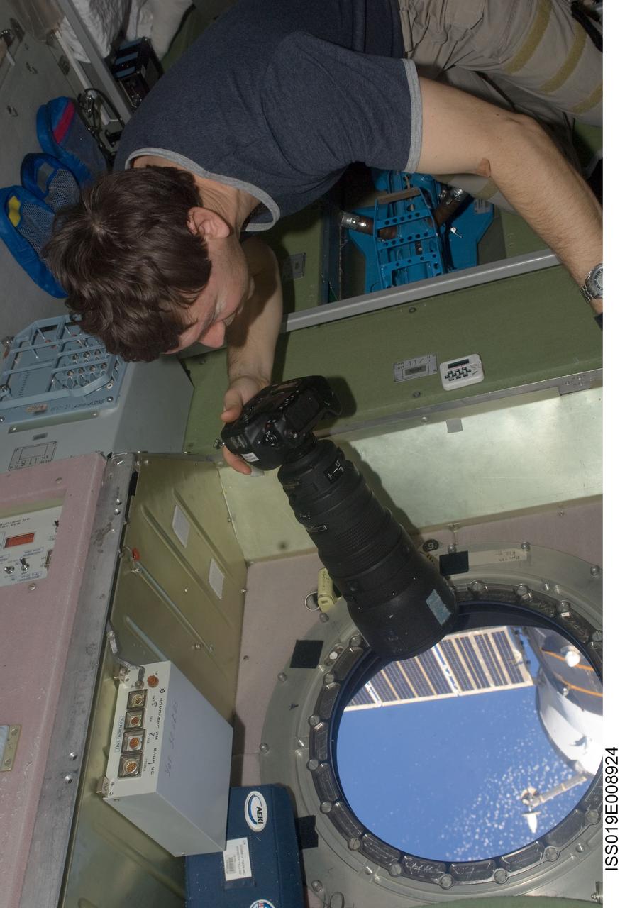 ISS019-E-008924 (19 April 2009) --- Astronaut Michael Barratt, Expedition 19/20 flight engineer, uses a still camera at a window in the Zvezda Service Module of the International Space Station.