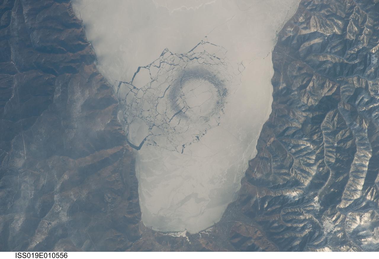 ISS019-E-010556 (23 April 2009) --- A circle in thin ice in Lake Baikal, Russia is featured in this image photographed by an Expedition 19 crewmember on the International Space Station. Late in April 2009, astronauts aboard the station observed a strange circular area of thinned ice (dark in color, with a diameter of about 4.4 kilometers) in the southern end of Lake Baikal in southern Siberia. Lake Baikal is unique in many regards. It is the largest (by volume) and deepest (1,637 meters at the deepest point) fresh water lake on Earth and, as a World Heritage Site, is considered one of Russia?s environmental jewels. The lake?s long, thin and deep profile results from its location in the Baikal Rift valley in Siberia. According to scientists, it is also one of the world?s oldest lakes (25-30 million years old); it contains up to 7 kilometers of sediment deposited on the bottom, and is home to an amazing array of plants and animals, many being found only in Lake Baikal. The lake?s biodiversity includes fresh water seals and several species of fish that are not found elsewhere on Earth. Siberia is remote and cold; ice cover can persist into June. This detailed image shows a circle of thin ice, which is the focal point for ice break up in the very southern end of the lake. While the origin of the circles is unknown, the peculiar pattern suggests convection in the lake?s water column.  Ice cover changes rapidly at this time of year.  Within a day, the ice can melt almost completely, and then freeze again overnight. Throughout April, the circles are persistent ? they appear when ice cover forms, and then disappear as ice melts. The pattern and appearance suggests that the ice is quite thin.