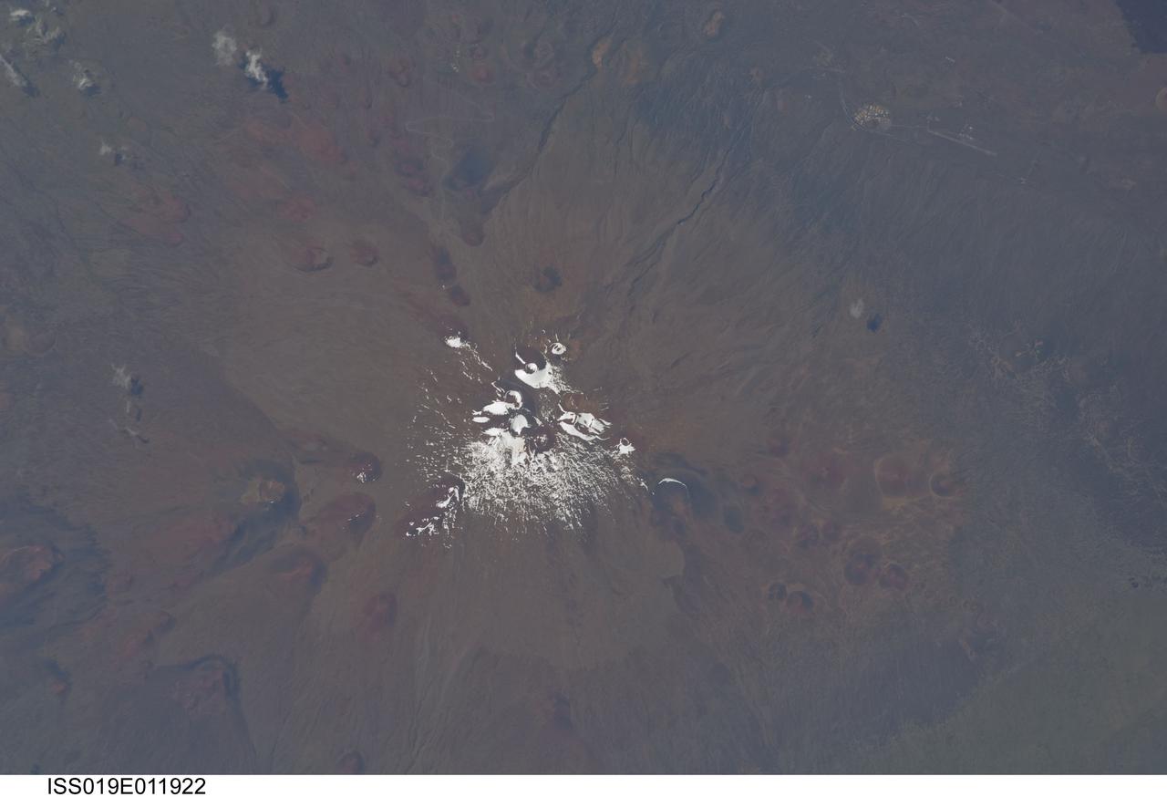 ISS019-E-011922 (28 April 2009) --- Mauna Kea Volcano in Hawaii is featured in this image photographed by an Expedition 19 crewmember on the International Space Station. The island of Hawaii is home to four volcanoes monitored by volcanologists ? Mauna Loa, Hualalai, Kilauea, and Mauna Kea. Mauna Kea is depicted in this view; of the four volcanoes, it is the only one that has not erupted during historical times. The Hawaiian Islands chain, together with the submerged Emperor Chain to the northwest, form an extended line of volcanic islands and seamounts that is thought to record passage of the Pacific Plate over a ?hotspot? (or thermal plume) in the Earth?s mantle. Areas of active volcanism in the southern Hawaiian Islands today mark the general location of the hotspot. This detailed photograph illustrates why the volcano is called Mauna Kea (?white mountain? in Hawaiian). While the neighboring Mauna Loa volcano is a classic shield volcano comprised of dark basaltic lava flows, Mauna Kea experienced more explosive activity during its last eruptive phase. This covered its basalt lava flows with pyroclastic deposits that are visible as the light brown area surrounding snow on the summit (center). Numerous small red to dark gray cinder cones are another distinctive feature of Mauna Loa. The cinder cones represent the most recent type of volcanic activity at the volcano. A small area of buildings and roadways at upper right is the Pohakuloa Training Area. This is the largest US Department of Defense facility in the state of Hawaii. The site is used for U.S. Army and Marine Corps exercises.