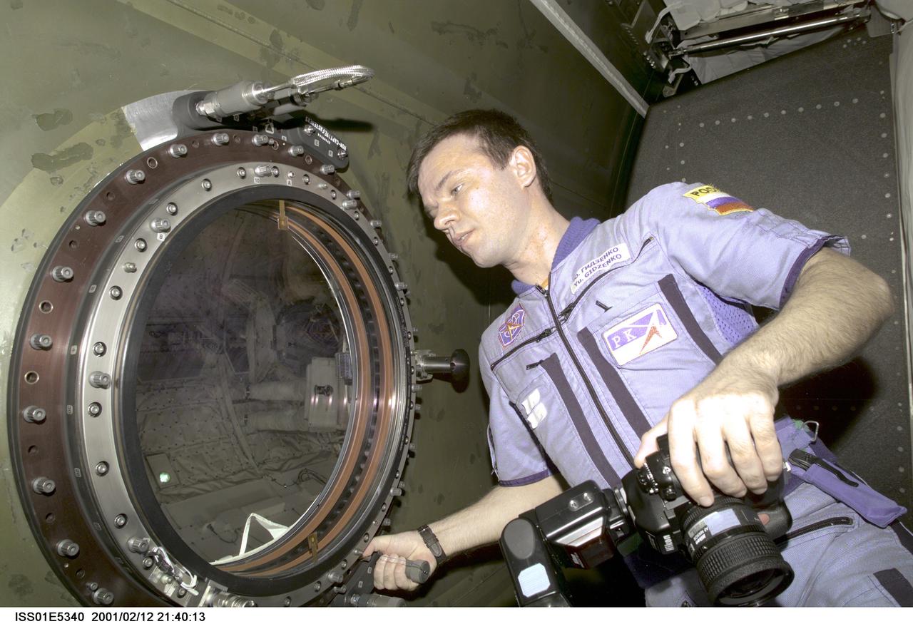 ISS01-E-5340 (12 February 2001) --- Cosmonaut Yuri P. Gidzenko, Expedition One's Soyuz commander, prepares to take pictures through the porthole in the Destiny laboratory. Gidzenko's photos will document parts of the second STS-98 space walk in the cargo bay of the Space Shuttle Atlantis. The legs of one of the space walkers can be seen through the window. Representing the Russian Aviation and Space Agency along with another cosmonaut, Gidzenko is part of a three man crew that intiated full-time habitation of the outpost in early November of 2000. This scene was recorded with a digital still camera.