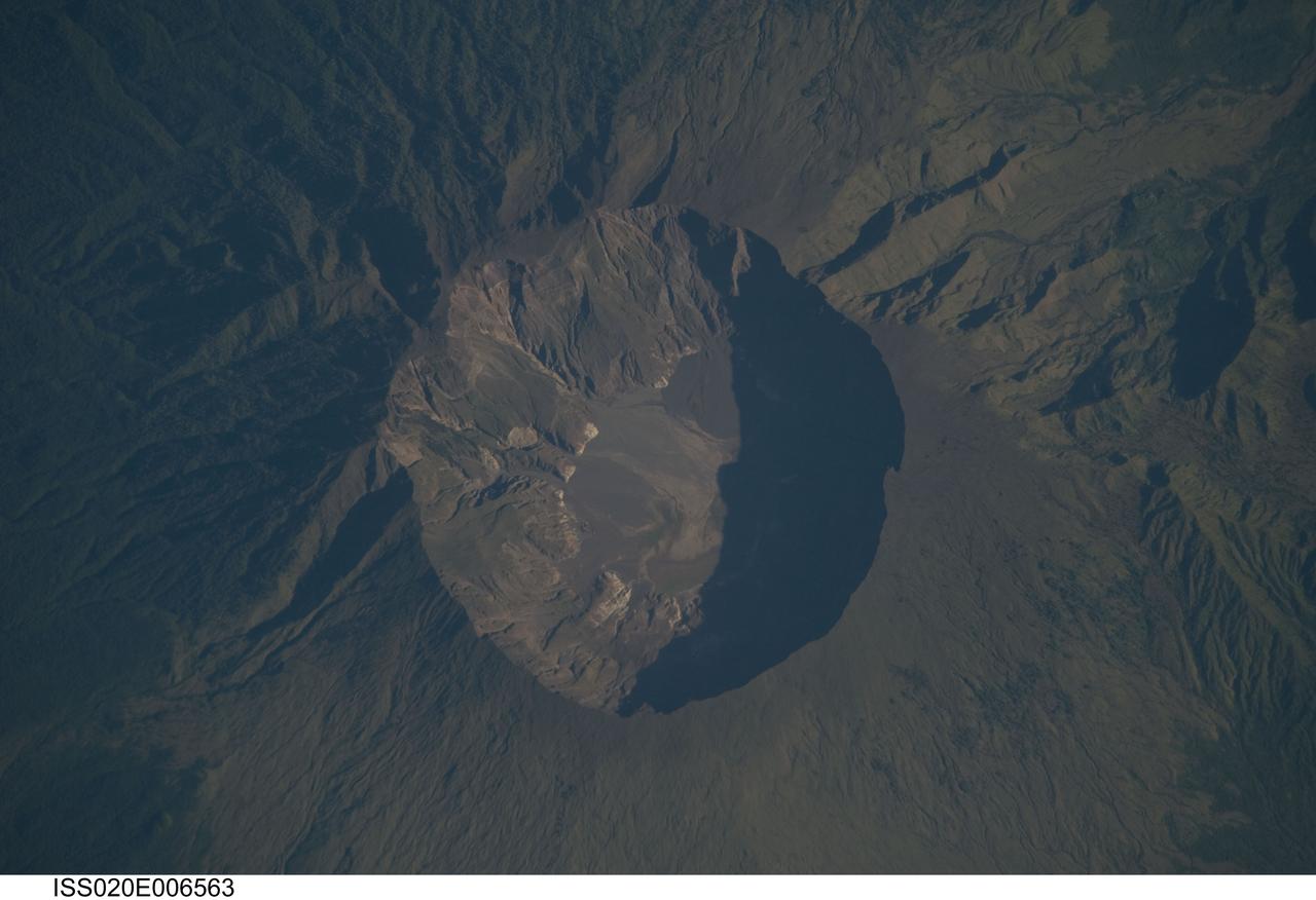 ISS020-E-006563 (3 June 2009) --- Mount Tambora Volcano, Sumbawa Island in Indonesia is featured in this image photographed by an Expedition 20 crew member on the International Space Station. On April 10, 1815 the Tambora volcano produced the largest eruption in history. An estimated 150 cubic kilometers of tephra ? exploded rock and ash ? was produced, with ash from the eruption recognized at least 1,300 kilometers away to the northwest. While the April 10 eruption was catastrophic, historical records and geological analysis of eruption deposits indicate that the volcano had been active between 1812 and 1815. Enough ash was input into the atmosphere from the April 10 eruption to reduce incident sunlight on Earth?s surface and cause global cooling, resulting in the 1816 ?year without a summer?. This detailed photograph depicts the summit caldera of the volcano. The huge caldera ? six kilometers in diameter and 1,100 meters deep ? formed when Tambora?s estimated 4,000 meter-high peak was removed, and the magma chamber below emptied, during the April 10 eruption. Today the crater floor is occupied by an ephemeral fresh-water lake, recent sedimentary deposits, and minor lava flows and domes emplaced during the 19th and 20th centuries. Layered tephra deposits are visible along the northwestern crater rim. Active fumaroles, or steam vents, are still present within the caldera. In 2004 scientists discovered the remains of a village and two adults buried under approximately three meters of ash in a gully on Tambora?s flank - remnants of the former Kingdom of Tambora preserved by the 1815 eruption that destroyed it. The similarity of the Tambora remains to those associated with the 79 AD eruption of Mount Vesuvius has led to the site being called ?the Pompeii of the East.?
