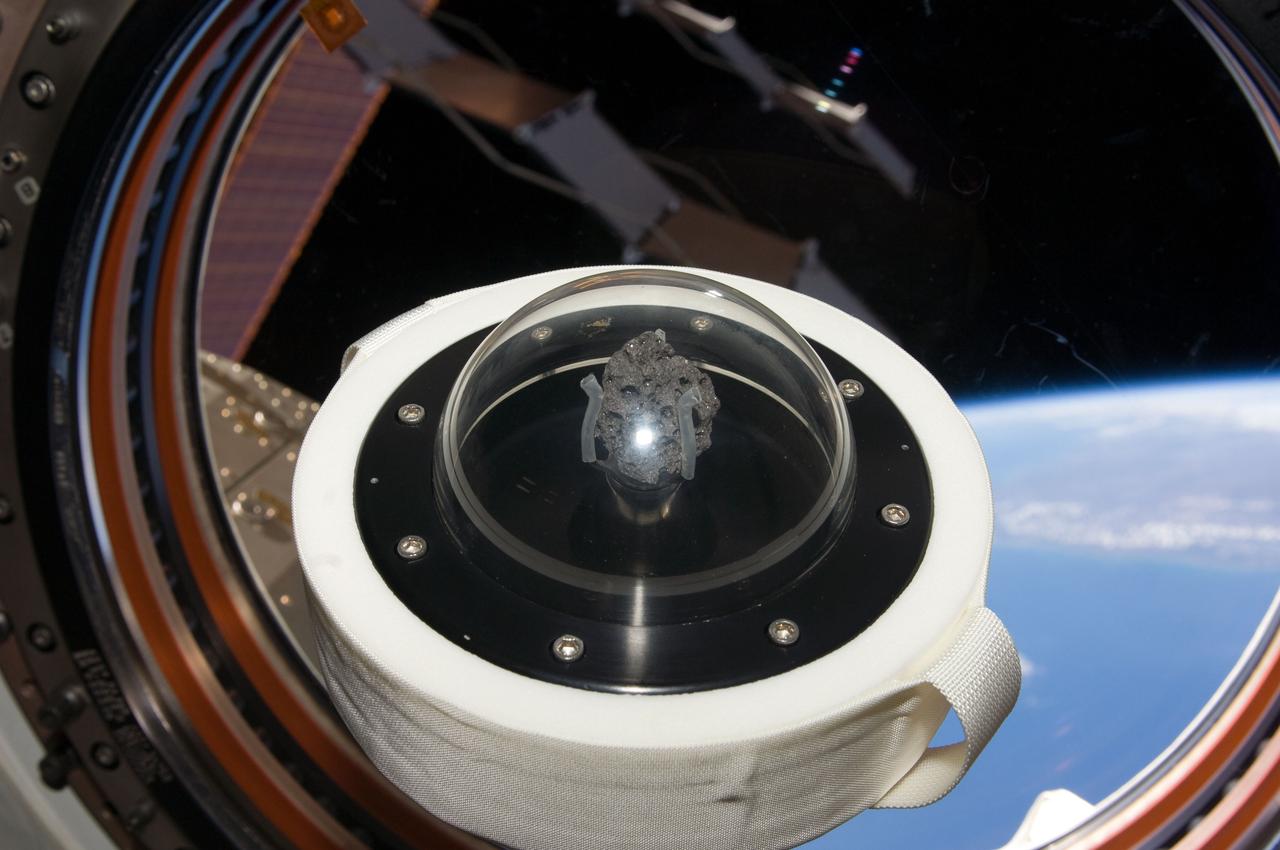 ISS020-E-14196 (FOR RELEASE 21 JULY 2009) --- A moon rock brought to Earth by Apollo 11, humans? first landing on the moon in July 1969, is shown as it floats aboard the International Space Station. Part of Earth can be seen through the window. The 3.6 billion year-old lunar sample was flown to the station aboard Space Shuttle mission STS-119 in April 2009 in honor of the July 2009 40th anniversary of the historic first moon landing. The rock, lunar sample 10072, was flown to the station to serve as a symbol of the nation?s resolve to continue the exploration of space. It will be returned on shuttle mission STS-128 to be publicly displayed.