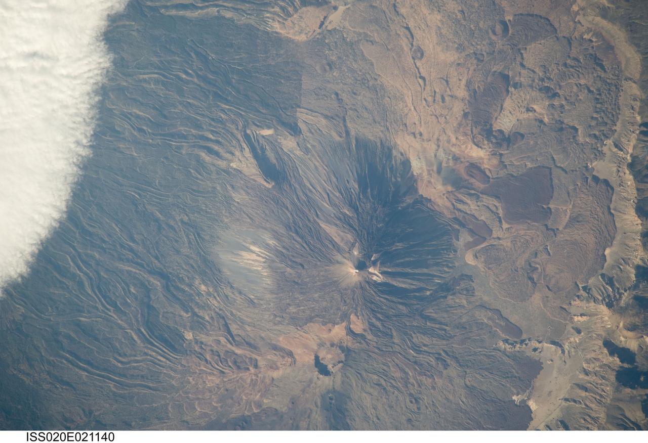ISS020-E-021140 (15 July 2009) --- Teide Volcano on the Canary Islands of Spain is featured in this image photographed by an Expedition 20 crew member on the International Space Station. This detailed photograph features two stratovolcanoes ? Pico de Teide and Pico Viejo ? located on Tenerife Island, part of the Canary Islands of Spain. Stratovolcanoes are steep-sided; typically conical structures formed by interlayered lavas and fragmented rock material from explosive eruptions. Pico de Teide has a relatively sharp peak, whereas an explosion crater forms the summit of Pico Viejo. The two stratovolcanoes formed within an even larger volcanic structure known as the Las Ca?adas caldera ? a large collapse depression typically formed when a major eruption completely empties the underlying magma chamber of a volcano. The last eruption of Teide occurred in 1909. NASA scientists point out sinuous flow levees marking individual lava flows. The scientists consider the flow levees as perhaps the most striking volcanic features visible in the image. Flow levees are formed when the outer edges of a channelized lava flow cool and harden while the still-molten interior continues to flow downhill ? numerous examples radiate outwards from the peaks of both Pico de Teide and Pico Viejo. Brown to tan overlapping lava flows and domes are visible to the east-southeast of the Teide stratovolcano. Increased seismicity, carbon dioxide emissions, and fumarolic activity within the Las Ca?adas caldera and along the northwestern flanks of the volcano were observed in 2004. Monitoring of the volcano to detect renewal of activity is ongoing.