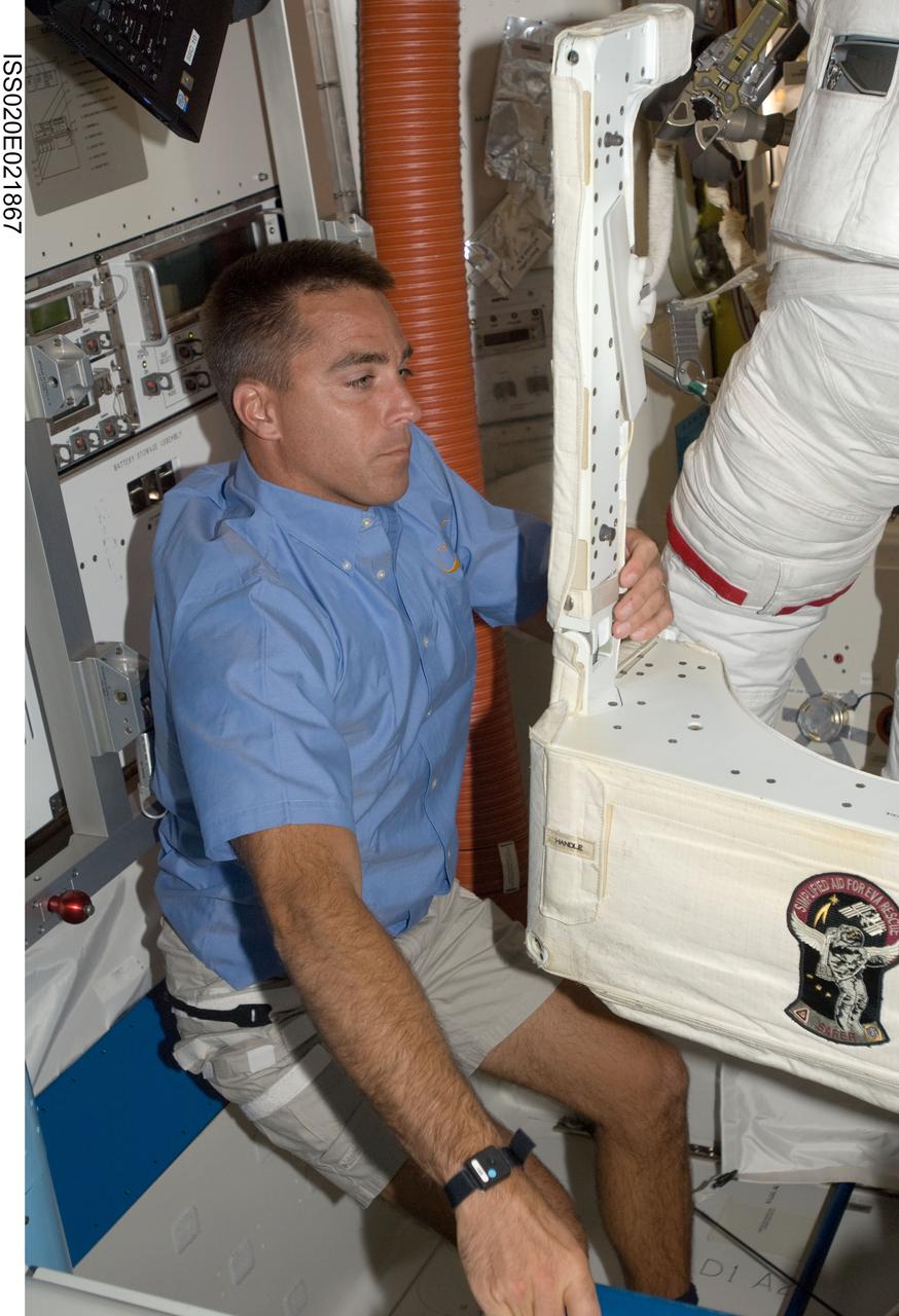 ISS020-E-021867 (18 July 2009) --- Astronaut Christopher Cassidy, STS-127 mission specialist, assists astronaut Dave Wolf (partially pictured), mission specialist, with the backpack for his extravehicular mobility unit or space suit prior to airlock egress. Astronauts Wolf and Tim Kopra later completed the first of five scheduled space walks to be spread over the next several days.
