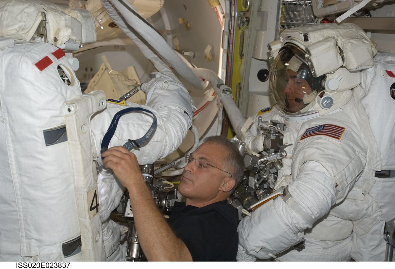 ISS020-E-023837 (24 July 2009) --- Astronaut Dave Wolf assists astronaut Tom Marshburn with his extravehicular mobility unit spacesuit in the joint airlock, while astronaut Christopher Cassidy stands suited and almost ready at right. The two were about to participate in the July 24 flight day 10 spacewalk, and they are scheduled to wrap up the EVA work with a fifth overall session on July 27. The three mission specialists are part of a 13-member aggregation of astronauts and cosmonauts currently onboard the orbital outpost while its crew of six plays host to Endeavour's crew of seven.