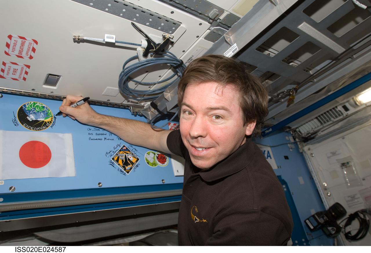 ISS020-E-024587 (25 July 2009) --- Astronaut Michael Barratt, Expedition 19/20 flight engineer, signs the Expedition 19 patch in the Kibo laboratory, which was added to the growing collection of insignias representing crews who have lived and worked on the International Space Station.