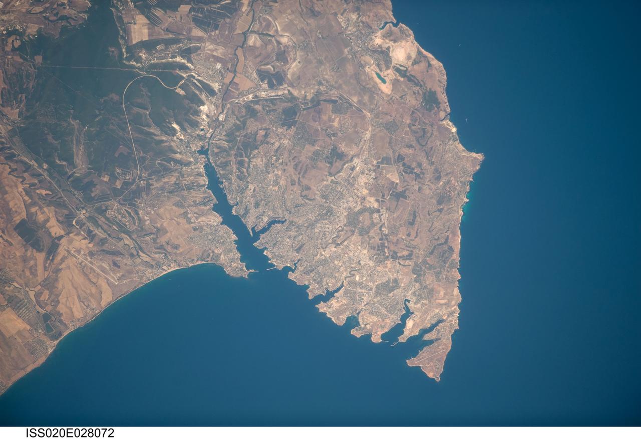 ISS020-E-028072 (5 Aug. 2009) --- Sevastopol, Ukraine is featured in this image photographed by an Expedition 20 crew member on the International Space Station. The port city of Sevastopol is located in southernmost Ukraine on the Crimean Peninsula. The city is an important naval base due to the numerous inlets and bays along the coastline (bottom center). During the Cold War, the city was the base of the Soviet Black Sea Fleet, but now services vessels of both the Ukraine and Russia. The main economy of the city is based on trade and shipbuilding, but Sevastopol is also a popular tourist and resort destination for visitors from the Commonwealth of Independent Countries (formed from former Soviet Republics). This photograph highlights the jagged coastline of the southern Crimean Peninsula and the various docking areas of Sevastopol. The urban area is light gray, and is bounded to the north and west by the Black Sea, to the south by vegetated (light green) and fallow (tan) agricultural fields, and to the east by the city of Inkerman and green vegetated uplands to the northwest of the Crimean Mountains. The city of Balaklava to the south houses another relic of the Cold War ? an underground Soviet submarine base that is now open to the public as a monument. The Chernaya River issues into the Black Sea near Inkerman, flowing into the Sevastopol Inlet to the west.