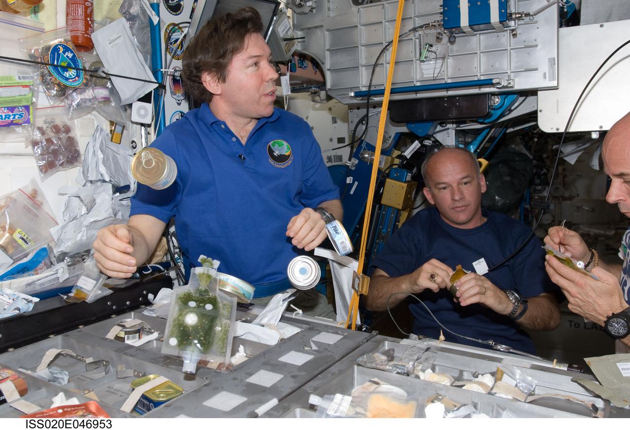 ISS020-E-046953 (5 Oct. 2009) --- NASA astronauts Michael Barratt (left), Expedition 19/20 flight engineer; and Jeffrey Williams, Expedition 21 flight engineer and Expedition 22 commander; along with spaceflight participant Guy Laliberte (mostly out of frame at right), share a meal at the galley in the Unity node of the International Space Station.