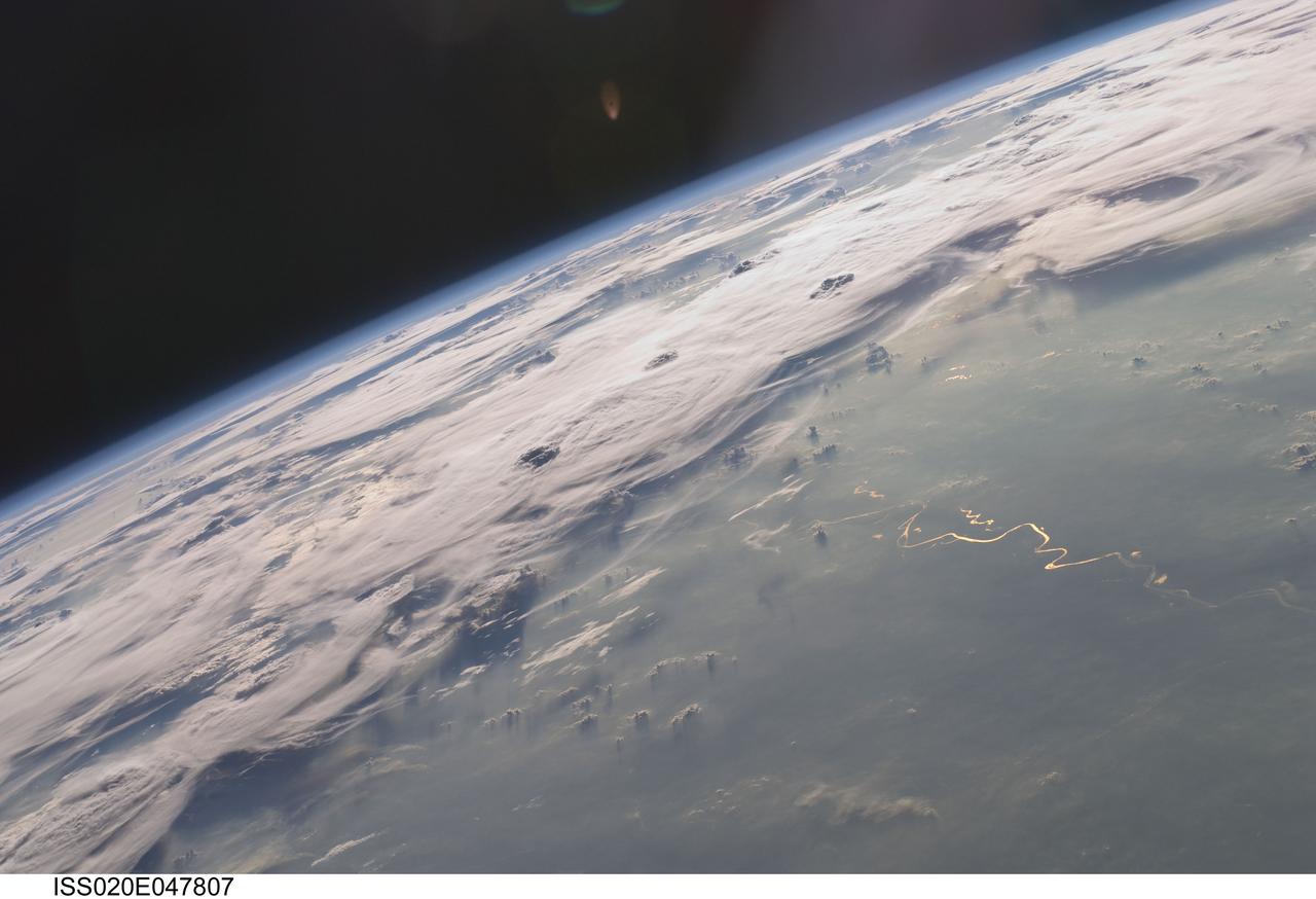 ISS020-E-047807 (6 Oct. 2009) --- Thunderstorms on the Brazilian horizon are featured in this image photographed by an Expedition 20 crew member on the International Space Station. A picturesque line of thunderstorms and numerous circular cloud patterns filled the view as the station crew members looked out at the limb and atmosphere (blue line on the horizon) of Earth. This region displayed in the photograph (top) includes an unstable, active atmosphere forming a large area of cumulonimbus clouds in various stages of development. The crew was looking west southwestward from the Amazon Basin, along the Rio Madeira, toward Bolivia when the image was taken. The distinctive circular patterns of the clouds in this view are likely caused by the aging of thunderstorms. Such ring structures often form during the final stages of a storm?s development as their centers collapse. Sunglint is visible on the waters of the Rio Madeira and Lago Acara in the Amazon Basin. Widespread haze over the basin gives the reflected light an orange hue. The Rio Madeira flows northward and joins the Amazon River on its path to the Atlantic Ocean. Scientists believe that a large smoke plume near the bottom center of the image may explain one source of the haze.