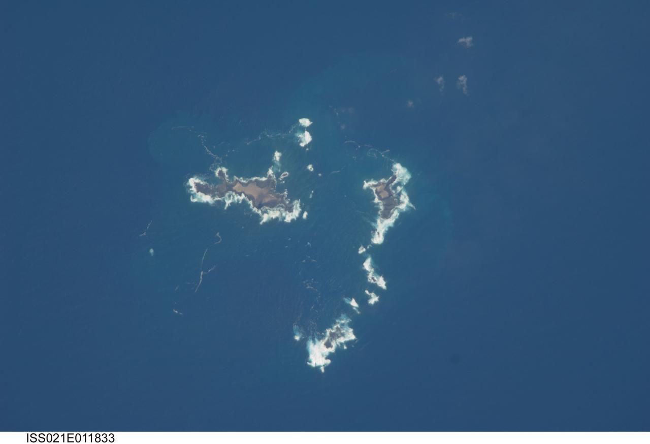 ISS021-E-011833 (22 Oct. 2009) --- The southern Savage Islands in the Atlantic Ocean are featured in this image photographed by an Expedition 21 crew member on the International Space Station. The Savage Islands, or Ilhas Selvagens in Portuguese, comprise a small archipelago in the eastern North Atlantic Ocean between the archipelago of Madeira to the north and the Canary Islands to the south. Like other island groups, the Savage Islands are thought to have been produced by volcanism related to a mantle plume or ?hot spot?. Mantle plumes are relatively fixed regions of upwelling magma that can feed volcanoes on an overlying tectonic plate. Active volcanoes form over the plume, and become dormant as they are carried away on the moving tectonic plate. Scientists believe that over geologic time, this creates a line of older extinct volcanoes, seamounts, and islands extending from the leading active volcanoes that are currently over the plume. This view illustrates the smaller and more irregularly-shaped Ilheus do Norte, Ilheu de Fora, and Selvagem Pequena. Spain and Portugal both claim sovereignty over the Savage Islands. All of the islands of the archipelago are ringed by bright white breaking waves along the fringing beaches. Coral reefs that surround the Savage Islands make it very difficult to land boats there, and there is no permanent settlement on the islands.