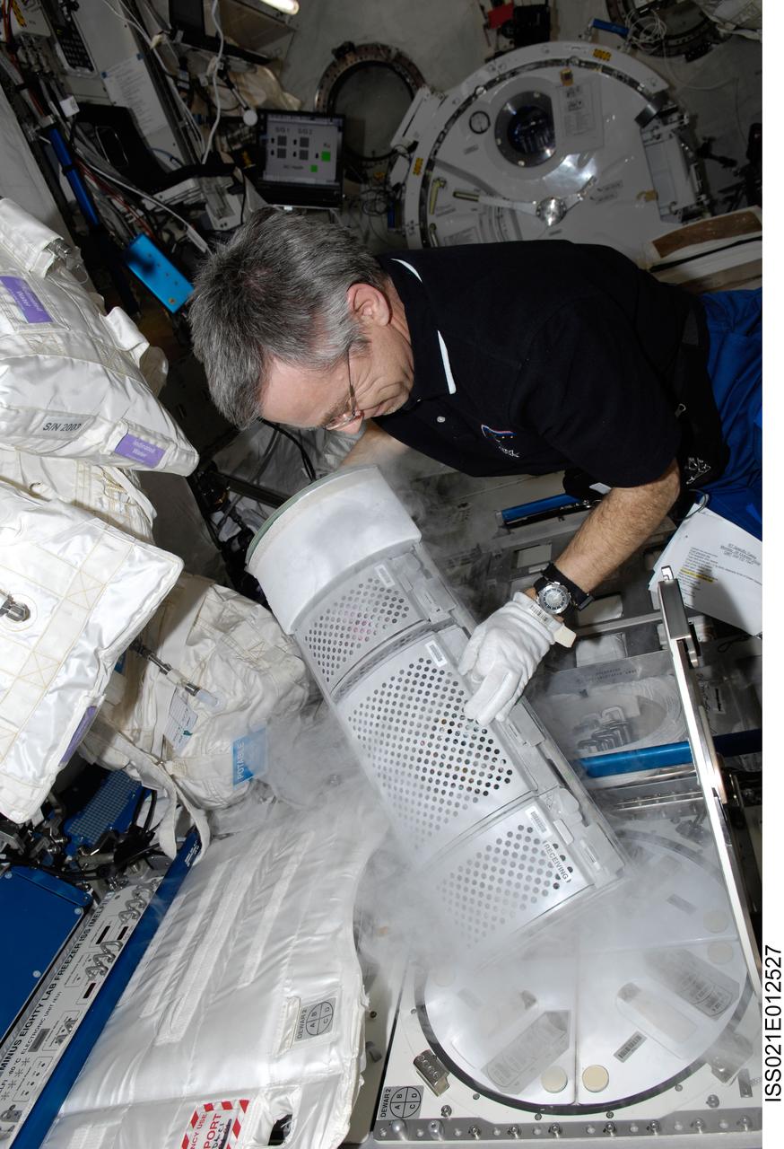 ISS021-E-012527 (26 Oct. 2009) --- Canadian Space Agency astronaut Robert Thirsk, Expedition 21 flight engineer, removes a dewar tray from the Minus Eighty Laboratory Freezer for ISS (MELFI) in order to insert biological samples into the trays in the Kibo laboratory of the International Space Station.