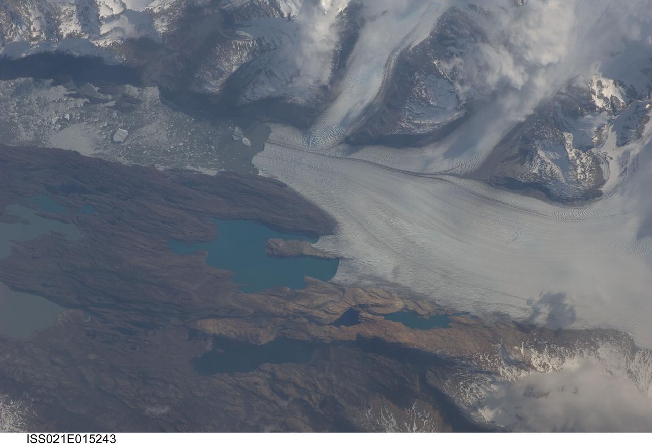 ISS021-E-015243 (25 Oct. 2009) --- Upsala Glacier, Argentina is featured in this image photographed by an Expedition 21 crew member on the International Space Station. The Southern Patagonian Ice Field of Argentina and Chile hosts some of the most spectacular glaciers in the world, and is second only to Antarctica in size. This detailed photograph illustrates the terminus of Upsala Glacier, located on the eastern side of the ice field. This glacier is the third largest in the Southern Patagonian Ice Field and, like most other glaciers in the region, has experienced significant retreat over the past century. This image was taken during spring in the Southern Hemisphere, and calving of icebergs ? release of chunks of ice from the glacier terminus as it enters the waters of Lake Argentina - is visible at left. Two icebergs are of particular interest, as they retain fragments of the moraine that forms a dark line along the upper surface of the glacier. Moraines of the type visible in this image are formed from coarse rock and soil debris that accumulates along the front and sides of a flowing glacier; much like a bulldozer blade pushes material in front of it. When two glaciers merge together (center), debris in moraines along their edges can now form a medial moraine that is drawn out along the upper surface of the new ice mass. These moraines can be carried intact to the terminus and included in icebergs that then float away, dropping the coarse debris as the iceberg melts. While the icebergs produced by Upsala Glacier do not reach an ocean, there are many current glaciers ? as well as glaciers and ice sheets that existed in the geologic past ? capable of producing ocean-going icebergs. This process is thought to be recorded in the geologic record as layers or lenses of coarse, land-derived sediments within finer grained sea floor sediments that are located far from any current (or former) coastline.