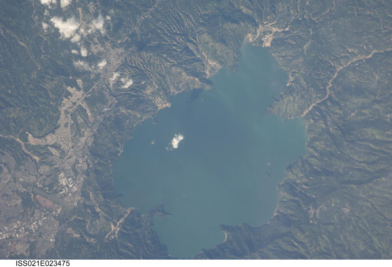 ISS021-E-023475 (11 Nov. 2009) --- Lake Ilopango, El Salvador is featured in this image photographed by an Expedition 21 crew member on the International Space Station. The Central American country of El Salvador occupies a land area nearly the same as the US State of Massachusetts, and includes numerous historically active volcanoes. This detailed photograph highlights the Ilopango Caldera that is located approximately 16 kilometers to the east of the capital city of San Salvador. Calderas are the geologic record of powerful volcanic eruptions that empty out a volcano?s magma chamber ? following the eruption, the overlying volcanic structure collapses into the newly-formed void, leaving a large crater-like feature (the caldera). The last caldera-forming eruption at Ilopango occurred during the 5th century AD; it was a powerful event that produced pyroclastic flows that destroyed early Mayan cities in the region. Later volcanic activity included the formation of several lava domes within the lake-filled caldera and near the shoreline. The only historical eruption at Ilopango took place in 1879-80. This activity resulted in the formation of a lava dome in the center of Lake Ilopango, the summit of which forms small islets today known as Islas Quemadas. The city of Ilopango borders the lake to the west (left) while green vegetated hillslopes ring the rest of the shoreline.  White patchy cumulus clouds are also visible in the image (center and upper left).