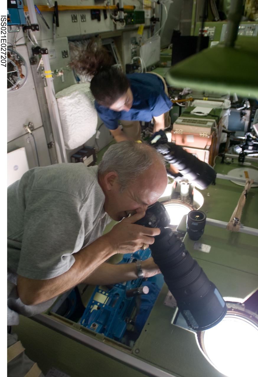 ISS021-E-027207 (15 Nov. 2009) --- NASA astronauts Jeffrey Williams and Nicole Stott, both Expedition 21 flight engineers, use still cameras at windows in the Zvezda Service Module of the International Space Station.