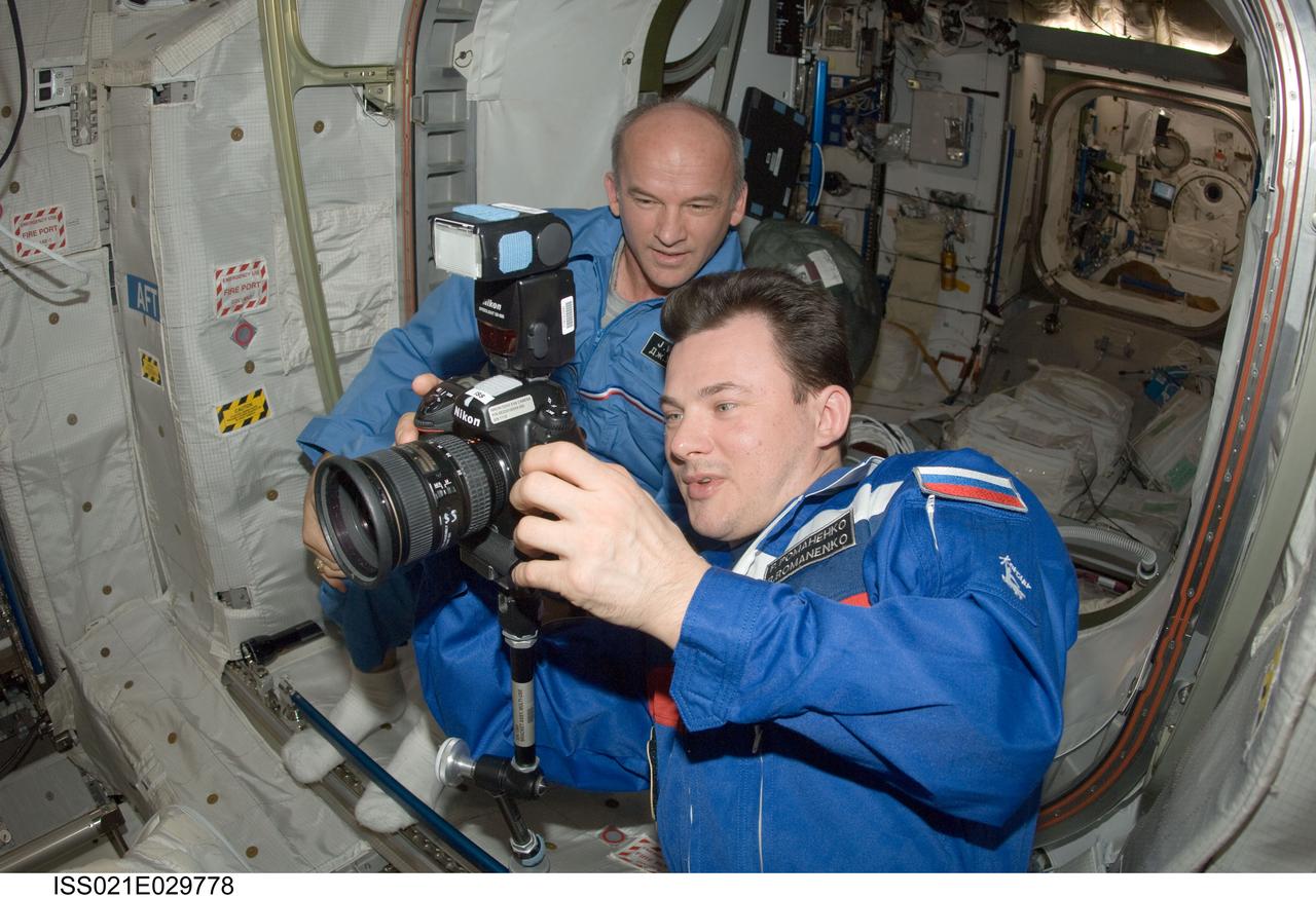 ISS021-E-029778 (17 Nov. 2009) --- Russian cosmonaut Roman Romanenko, Expedition 21 flight engineer, uses a still camera in the Columbus laboratory of the International Space Station while NASA astronaut Jeffrey Williams, flight engineer, looks on.