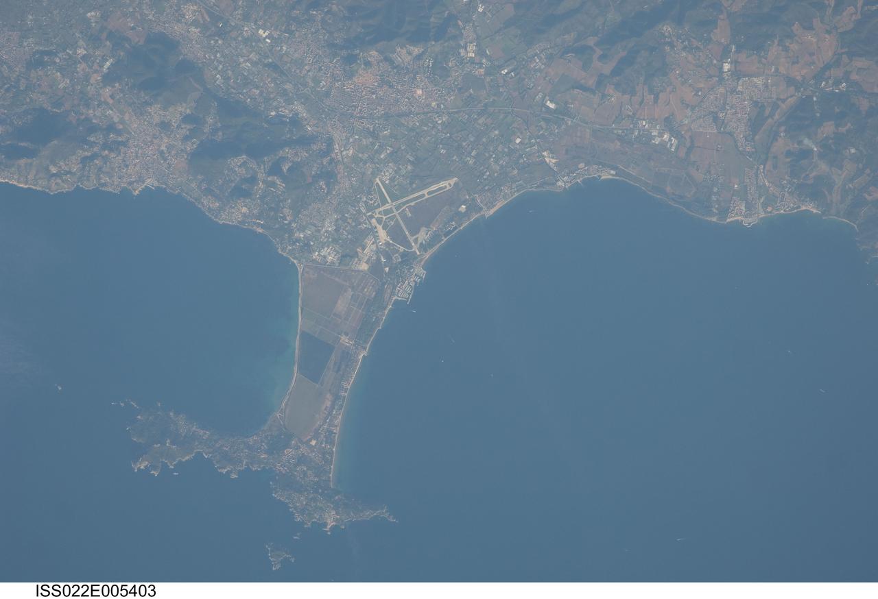 ISS022-E-005403 (2 Dec. 2009) --- Giens Peninsula, France is featured in this image photographed by an Expedition 22 crew member on the International Space Station. This detailed image depicts the Giens Peninsula located along the Mediterranean coastline of France. The peninsula is part of the Cote d?Azur, also known as the French Riviera, the coastal region bounded by the Rhone River to the west, to the north by the Rhone Alps, and the east by the Italian border. The peninsula itself, extended out southwards from the city of Hyeres to the resort community of Giens, is formed from two tombolos. A tombolo is a ridge of beach material (typically sand) built by wave action that connects an island to the mainland. Tombolos, like many coastal features, typically change dramatically over geologic time due to fluctuating sediment supply, coastal currents, sea levels and storm events. The tombolos of the Giens Peninsula have been modified by human activities including sand dune removal, construction of roadways, and replacement of the original sand by other materials. The long-term survival of these tombolos will be determined by the effects of these changes on the natural coastal processes, with potential sea level rise presenting an additional threat. In addition to Giens, three other urban areas are visible in this image; Carqueiranne, Hyeres, and La Londe-les-Maures. The urban areas are recognizable by both light pink rooftops and grey street grids. These contrast with green to brown vegetated areas including agricultural fields (between Hyeres and La Londe-les-Maures, top center) and dark green vegetated hillslopes (between Hyeres and Carqueiranne, top left). Small white dots and streaks in the Mediterranean Sea are actually yachts and other pleasure craft.