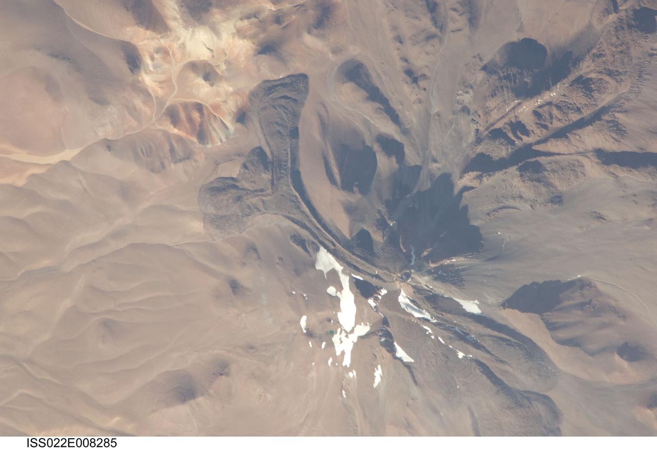 ISS022-E-008285 (9 Dec. 2009) --- Llullaillaco volcano on the Argentina-Chile border is featured in this image photographed by an Expedition 22 crew member on the International Space Station. The summit of Llullaillaco volcano has an elevation of 6,739 meters above sea level, making it the highest historically active volcano in the world. The current Llullaillaco stratovolcano ? a typically high, cone-shaped volcano built from successive layers of thick lava flows and eruption products like ash and rock fragments ? is built on top of an older stratovolcano. The last explosive eruption of the volcano occurred in 1877 based on historical records. This detailed photograph of Llullaillaco illustrates an interesting volcanic feature known as a coulee (top left). Coulees are formed from highly viscous, thick lavas that flow onto a steep surface; as they flow slowly downwards, the top of the flow cools and forms a series of parallel ridges oriented at 90 degrees to the direction of flow (somewhat similar in appearance to the pleats of an accordion). The sides of the flow can also cool faster than the center, leading to the formation of wall-like structures known as flow levees (center).