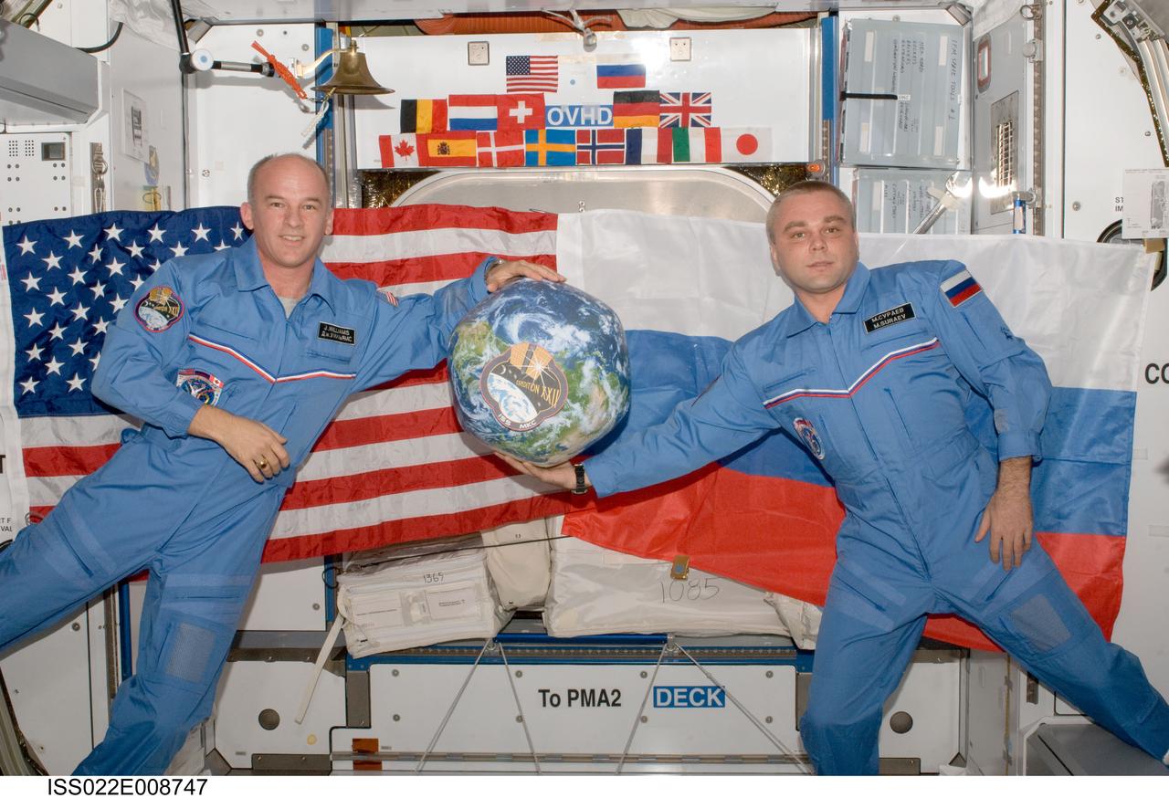 ISS022-E-008747 (13 Dec. 2009) --- NASA astronaut Jeffrey Williams (left), Expedition 22 commander; and Russian cosmonaut Maxim Suraev, flight engineer, hold a globe with the Expedition 22 logo during a segment of Rusalka video footage as part of Suraev’s "Live on ISS" program for the Russian Channel TVTs, via US assets (S-band & Ku-band). The event took place in the Harmony node of the International Space Station.