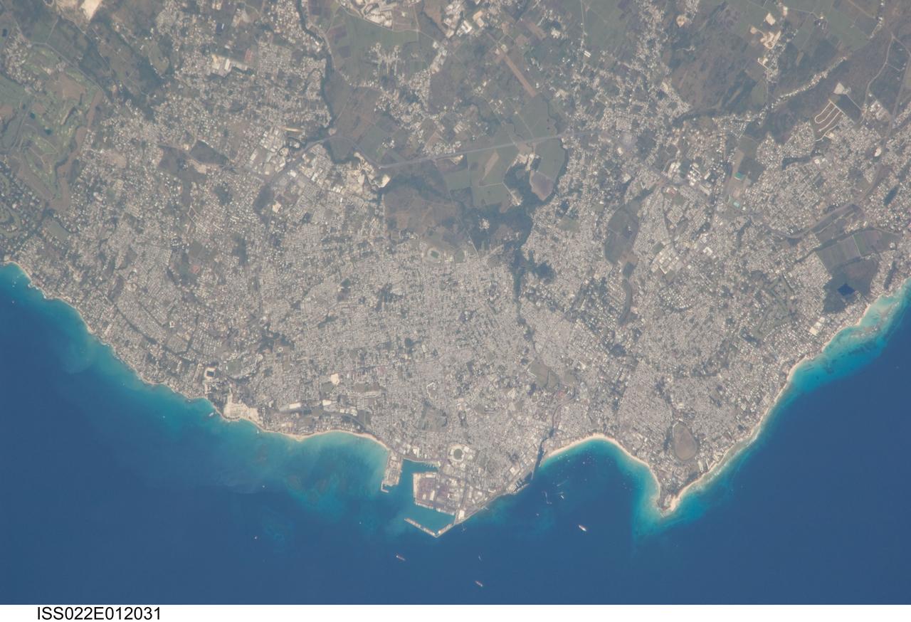 ISS022-E-012031 (16 Dec. 2009) --- Greater Bridgetown area, Barbados is featured in this image photographed by an Expedition 22 crew member on the International Space Station. Bridgetown is the capital city of the island nation of Barbados, located to the east of the Lesser Antilles Island chain. While Barbados is considered to be part of the Lesser Antilles, it is located within the western Atlantic Ocean rather than the Caribbean Sea region. Bridgetown is the largest city in Barbados in addition to being the seat of government. Barbados is a member of the British Commonwealth, and considers Queen Elizabeth II to be its constitutional monarch. Bridgetown, and the surrounding towns that make up the Greater Bridgetown area, is located along the southwestern coastline of the island. The metropolitan area is readily recognized in this image due to the gray and white rooftops and street grids (center) that contrast with green vegetated fields and riparian areas of the island?s interior to the northeast (top center). Bridgetown is a major port destination for both commercial and cruise ships serving the eastern Caribbean ? several ships are visible within Carlisle Bay. Water color in the image changes from light blue along the coastline ? indicating shallow water ? to the dark blue of deeper water away from the island.