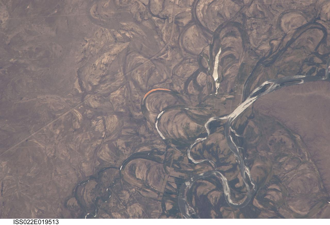 ISS022-E-019513 (4 Jan. 2010) --- The Rio Negro floodplain in Patagonia, Argentina is featured in this image photographed by an Expedition 22 crew member on the International Space Station. The Rio Negro is recognizable by astronaut crews from orbit as one of the most meandering rivers in South America. This is well illustrated in this view, where the entire river floodplain (approximately 10 kilometers wide) is covered with curved relics of channels known as meander scars. The main channel of the river, flowing south at this point?60 kilometers south of the city of Choele Choel  (not shown)?appears in partial sun glint at right. Sun glint occurs when light is reflected off a water surface directly back towards the viewer, imparting a silvery sheen to those areas. When meander scars contain water they are known as oxbow lakes, some of which are also highlighted by sun glint in the image. Meander scars show the numerous past positions of river bends, produced as the river snaked across the plain in the very recent geological past. The Rio Negro is a dramatic example of how mobile a river can be. The orange tint to the water in one of the oxbow lakes (center) could result from orange salt-loving algae. Their appearance here would be unusual since floodplain lakes are usually too fresh for algae blooms. But an explanation may lie in the location of the Rio Negro on the margin of Argentina?s arid Patagonian region with annual rainfall less than 12 inches (300 mm). Evaporation in this cloudless region could be high enough for some lakes to become salty. The Rio Negro flows generally southeast from the Andes Mts. to the Atlantic Ocean. Its floodplain supports the biggest pear- and apple-growing region of Argentina. Rectangular farm boundaries can be seen at bottom center. The river also hosts the world?s longest kayak regatta (653 kilometers), which lasts six days.