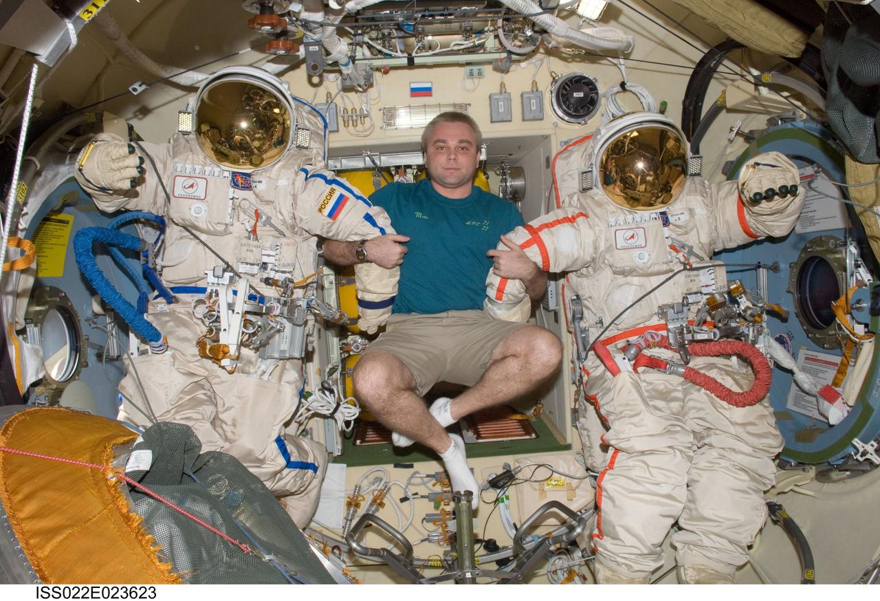 ISS022-E-023623 (11 Jan. 2010) --- Russian cosmonaut Maxim Suraev, Expedition 22 flight engineer, poses for a photo with two Russian Orlan spacesuits in the Pirs Docking Compartment of the International Space Station.
