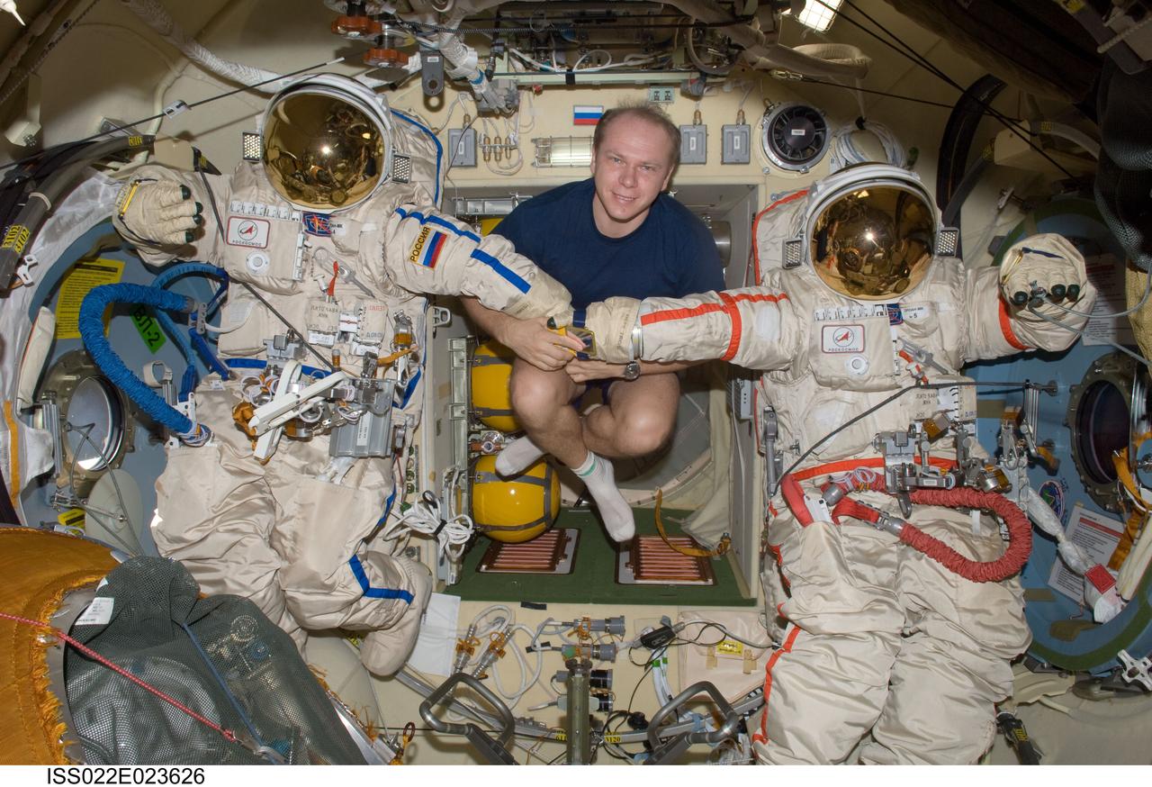 ISS022-E-023626 (11 Jan. 2010) --- Russian cosmonaut Oleg Kotov, Expedition 22 flight engineer, poses for a photo with two Russian Orlan spacesuits in the Pirs Docking Compartment of the International Space Station.