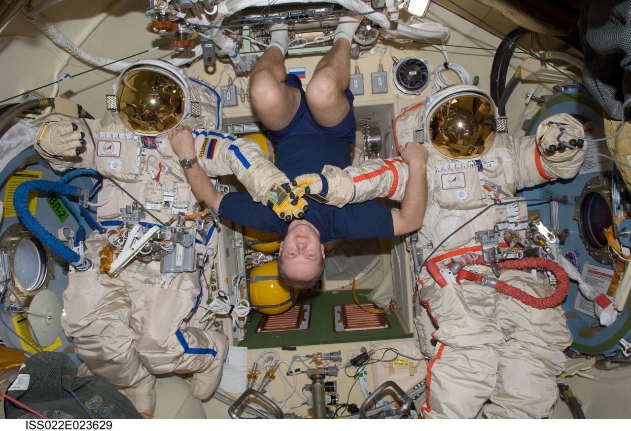 ISS022-E-023629 (11 Jan. 2010) --- Russian cosmonaut Oleg Kotov, Expedition 22 flight engineer, poses for a photo with two Russian Orlan spacesuits in the Pirs Docking Compartment of the International Space Station.