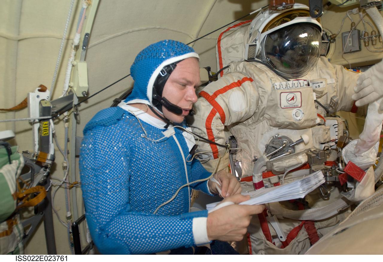 ISS022-E-023761 (12 Jan. 2010) --- Attired in a blue thermal undergarment that complements the Russian Orlan spacesuit, Russian cosmonaut Oleg Kotov, Expedition 22 flight engineer, reads a checklist in the Pirs Docking Compartment of the International Space Station.