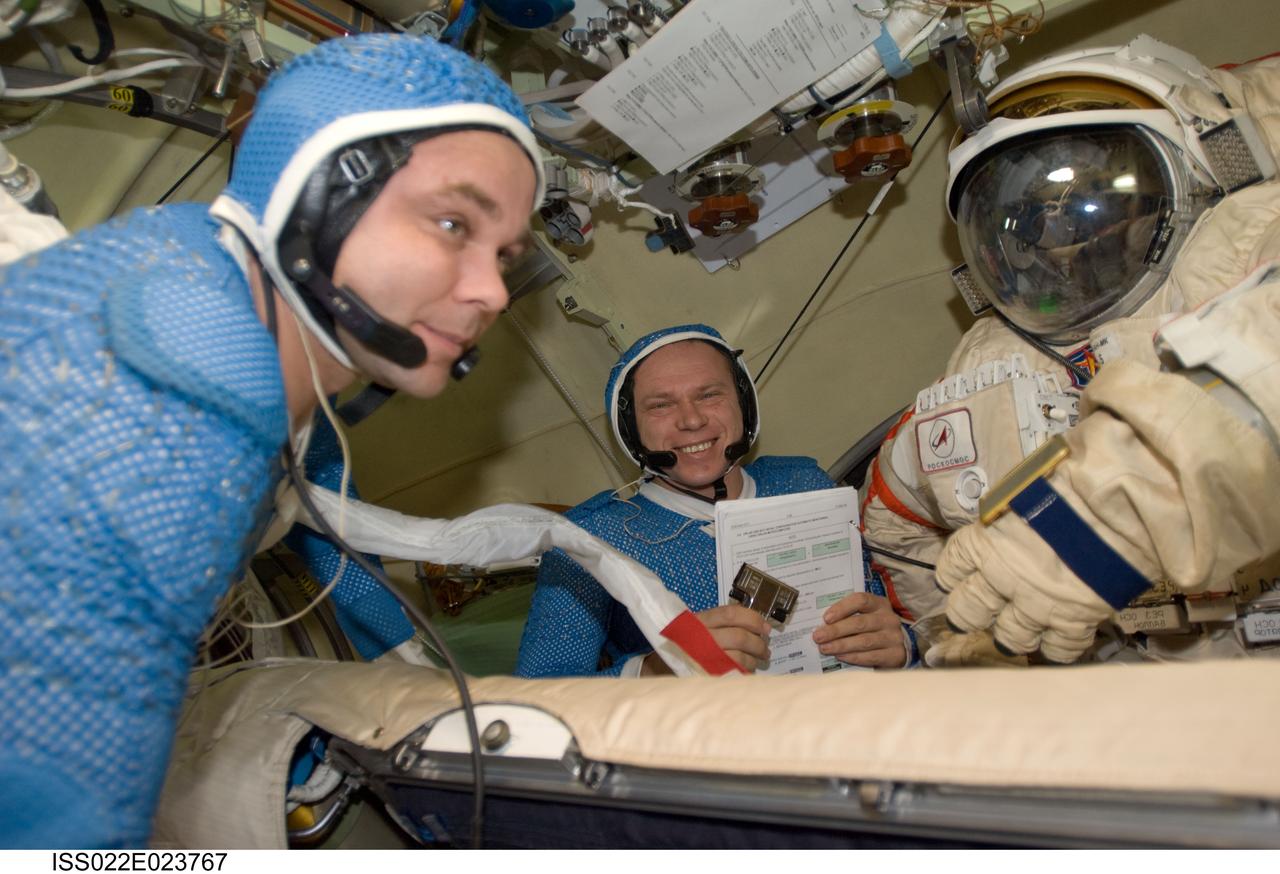 ISS022-E-023767 (12 Jan. 2010) --- Attired in blue thermal undergarments that complement the Russian Orlan spacesuit, Russian cosmonauts Maxim Suraev (foreground) and Oleg Kotov, both Expedition 22 flight engineers, prepare to don and check out their Orlan spacesuits in preparation for a spacewalk scheduled for Jan. 14 to outfit the new Poisk module for future Russian vehicle dockings.