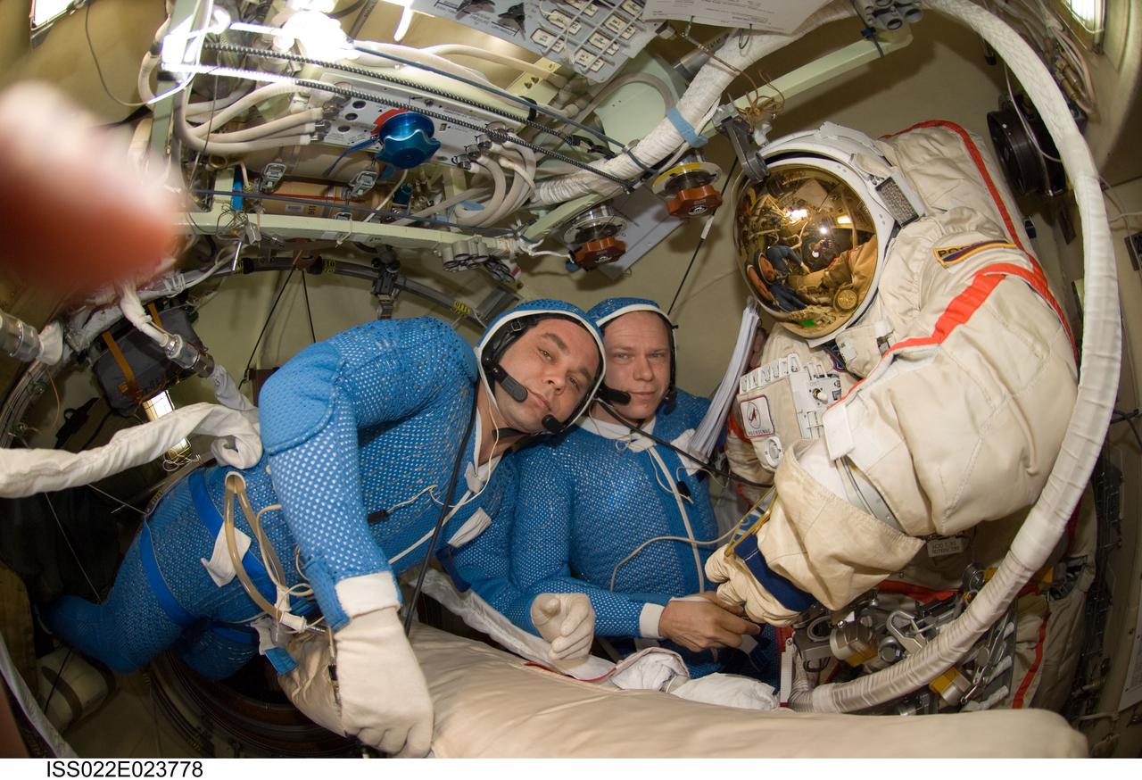 ISS022-E-023778 (12 Jan. 2010) --- Attired in blue thermal undergarments that complement the Russian Orlan spacesuit, Russian cosmonauts Maxim Suraev (left) and Oleg Kotov, both Expedition 22 flight engineers, prepare to don and check out their Orlan spacesuits in preparation for a spacewalk scheduled for Jan. 14 to outfit the new Poisk module for future Russian vehicle dockings.
