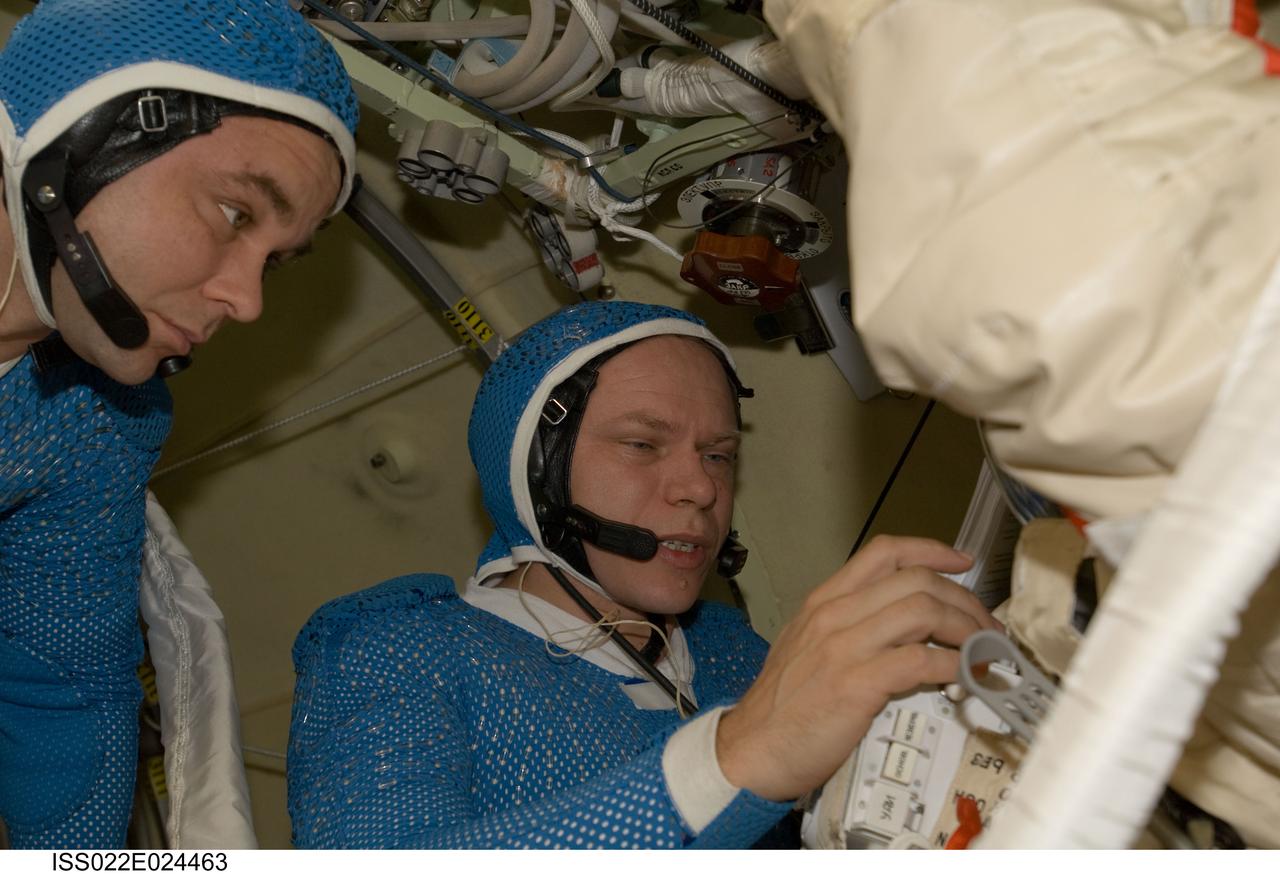 ISS022-E-024463 (12 Jan. 2010) --- Attired in blue thermal undergarments that complement the Russian Orlan spacesuit, Russian cosmonauts Maxim Suraev (left) and Oleg Kotov, both Expedition 22 flight engineers, prepare to don and check out their Orlan spacesuits in preparation for a spacewalk scheduled for Jan. 14 to outfit the new Poisk module for future Russian vehicle dockings.
