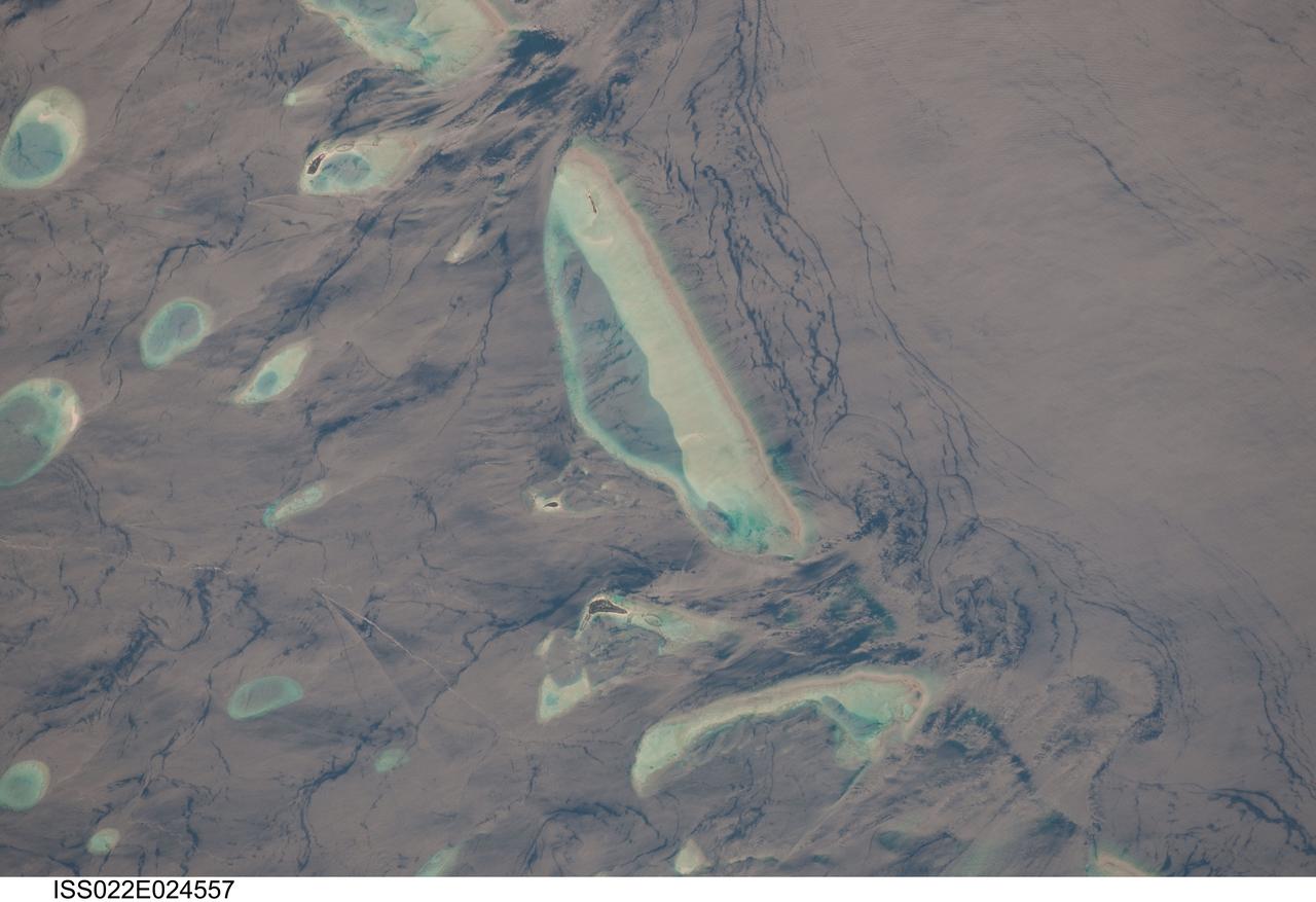 ISS022-E-024557 (12 Jan. 2010) --- Male Atoll and Maldive Islands in the Indian Ocean are featured in this image photographed by an Expedition 22 crew member on the International Space Station. This detailed photograph features one of the numerous atolls in the Maldive Island chain. The Maldives are an island nation, comprised of twenty-six atolls that stretch in a north-to-south chain for almost 900 kilometers southwest of the Indian subcontinent. The silvery, almost pink sheen on the normally blue water of the equatorial Indian Ocean is the result of sunglint. Sunglint occurs when sunlight is reflected off of a water surface directly back towards the observer ? in this case a crew member on the space station. Full sunglint in images typically results in bright silver to white coloration of the water surface. Sunglint images can have different hues depending on the roughness of the water surface and atmospheric conditions. They also can reveal numerous details of water circulation which are otherwise invisible. This image was taken during the Indian Ocean Northeast monsoon season - predominant winds in this area create sinuous surface water patterns on the leeward side, and between, the islets (left). A south-flowing current flows in the deeper water through the Maldives most of the year (right), with fan-shaped surface currents formed by local tides pulsing in and out of the shallow water near the islands (top and bottom). The largest island seen here (center) is 6 kilometers long, and is one of the outer ring of larger islands that make up the 70 kilometers-long, oval-shaped Male Atoll. Shores facing deeper water have well-defined beaches. Numerous small, elliptical coral reef islets are protected within the ring of shallow water to the northeast (left). These islets are mostly awash at high tide, with dry ground appearing in tiny patches only. A small boat was navigating between the islets at the time the image was taken as indicated by its v-shaped wake at bottom left. Images like these illustrate why the Republic of Maldives is one of the most outspoken countries in stressing the dangers of rising sea levels.