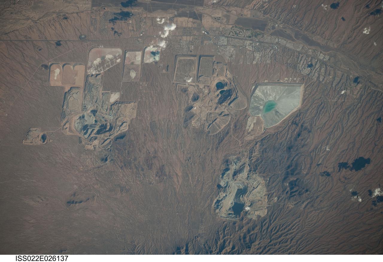 ISS022-E-026137 (14 Jan. 2010) --- Open Pit Mines in southern Arizona are featured in this image photographed by an Expedition 22 crew member on the International Space Station. The State of Arizona is the United States? largest producer of the metal copper, primarily mined from ore bodies known as porphyry copper deposits. Copper is a good conductor of electricity and heat, and is a vital element of virtually all of our electronic devices and components. A porphyry copper deposit is a geological structure formed by crystal-rich magma moving upwards through pre-existing rock layers. As the magma cools and crystallizes, it forms an igneous rock with large crystals embedded in a fine-grained matrix, known as porphyry. Hot fluids circulate through the magma and surrounding rocks via fractures, depositing copper-bearing and other minerals in characteristic spatial patterns that signal the nature of the ore body to a geologist. The most common approach to extracting metal-bearing ore from a porphyry copper deposit is by open-pit mining. For more details, please refer to http://earth.jsc.nasa.gov/EarthObservatory/OpenPitMinesSouthernArizona.htm.