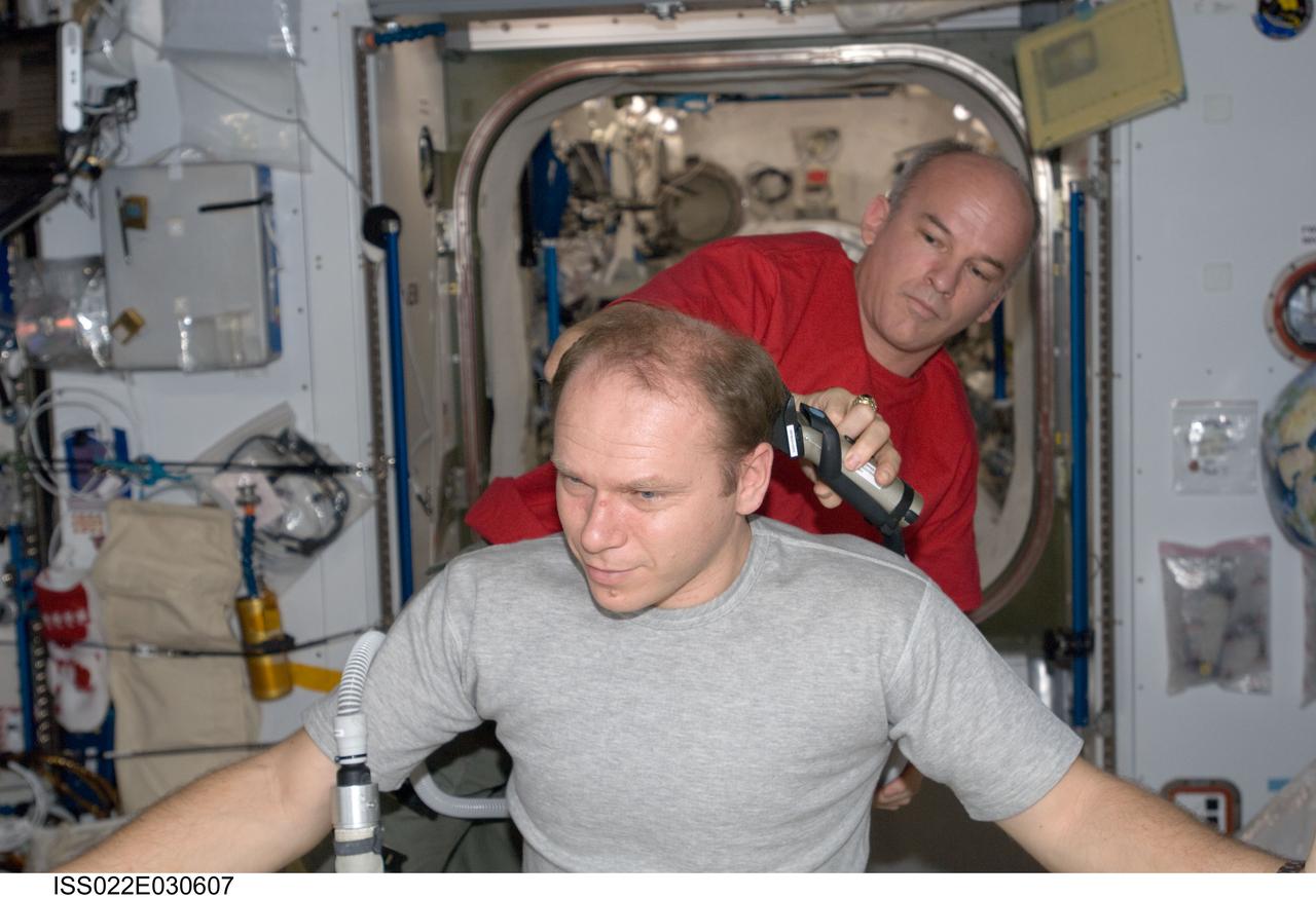 ISS022-E-030607 (19 Jan. 2010) --- NASA astronaut Jeffrey Williams, Expedition 22 commander, trims Russian cosmonaut Oleg Kotov’s hair in the Harmony node of the International Space Station. Williams used hair clippers fashioned with a vacuum device to garner freshly cut hair.