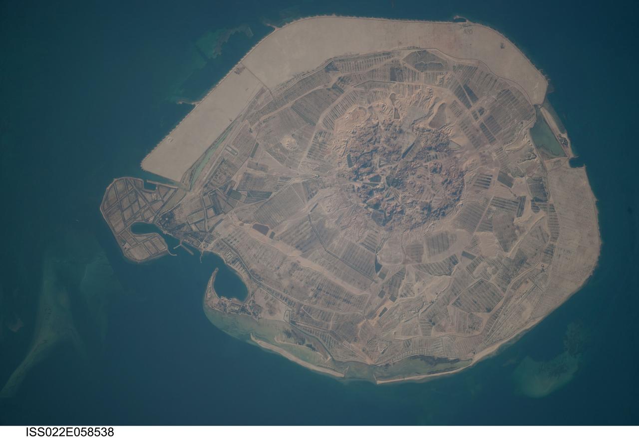 ISS022-E-058538 (31 Jan. 2010) --- Sir Bani Yas Island is featured in this image photographed by an Expedition 22 crew member on the International Space Station. Sir Bani Yas Island is located in the Persian Gulf near the western coastline of the United Arab Emirates (UAE). The approximately 14-kilometers x nine-kilometers island is the surface expression of a salt dome, and is one of several such islands in the Persian Gulf. During past periods of alternating wet and dry climate, sometimes involving areas with high rates of evaporation in enclosed basins, thick layers of salt minerals (such as halite ? common table salt, or gypsum ? a major component of wallboard) were deposited. These layers were subsequently buried by sediments; with enough overlaying material and depth of burial, the salt layers can begin to flow.  Salt has lower density than the surrounding rock and it tends to flow upwards, pushing up the overlaying layers of rock to form a salt dome. While many salt domes retain a cap of the youngest rock layers at the surface, in some cases the underlaying salt extrudes onto the surface. This photograph illustrates the varying character of surfaces on the island. The central mountains of Jebel Wahid (center) mark the location of the Sir Bani Yas salt dome. The dome has breached the surface but exposed salt - primarily gypsum - is removed by erosion, leaving a rugged, insoluble cap formed from fragments of the overlaying sedimentary and volcanic rocks. Sand and silt derived from the Jebel Wahid area and surrounding gravel cover forms beaches along the outer edge of the island.