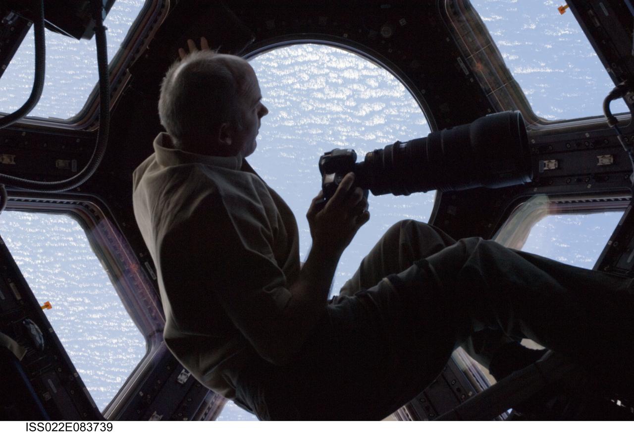ISS022-E-083739 (7 March 2010) --- While holding a still camera, NASA astronaut Jeffrey Williams, Expedition 22 commander, looks through a window in the Cupola of the International Space Station.
