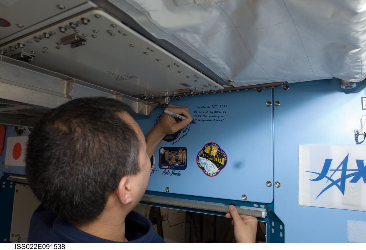 ISS022-E-091538 (12 March 2010) --- Japan Aerospace Exploration Agency (JAXA) astronaut Soichi Noguchi, Expedition 22 flight engineer, writes a note above the Expedition 22 insignia placed over the hatch in the Kibo laboratory of the International Space Station.