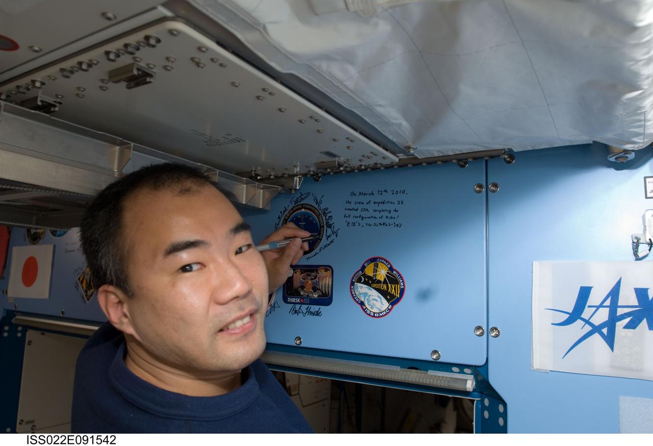 ISS022-E-091542 (12 March 2010) --- Japan Aerospace Exploration Agency (JAXA) astronaut Soichi Noguchi, Expedition 22 flight engineer, writes a note above the Expedition 22 insignia placed over the hatch in the Kibo laboratory of the International Space Station.