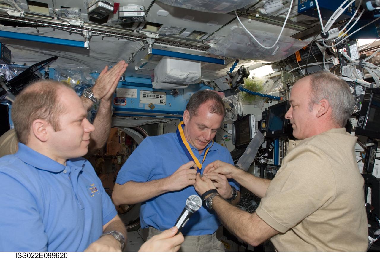 ISS022-E-099620 (17 March 2010) --- NASA astronaut Jeffrey Williams (right), Expedition 22 commander, presents the Army aviator award of St. Michael to fellow Army officer T.J. Creamer (center), Expedition 22/23 flight engineer, prior to the start of the ceremony of Changing-of-Command from Expedition 22 to Expedition 23. Russian cosmonaut Oleg Kotov, Expedition 22 flight engineer and Expedition 23 commander, holds a microphone at left.