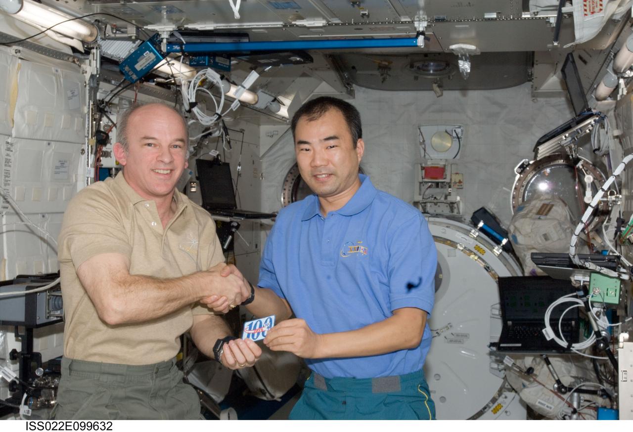 ISS022-E-099632 (17 March 2010) --- NASA astronaut Jeffrey Williams (left), Expedition 22 commander; and Japan Aerospace Exploration Agency (JAXA) astronaut Soichi Noguchi, Expedition 22/23 flight engineer, shake hands while holding a 100-day patch in the Kibo laboratory of the International Space Station.