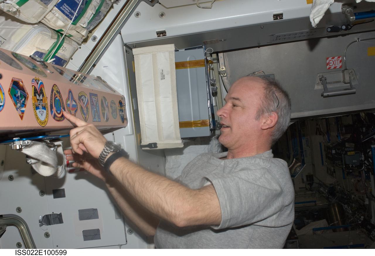 ISS022-E-100599 (17 March 2010) --- NASA astronaut Jeffrey Williams, Expedition 22 commander, looks at the various mission insignias placed in the Unity node of the International Space Station after placing the Expedition 22 insignia among them.